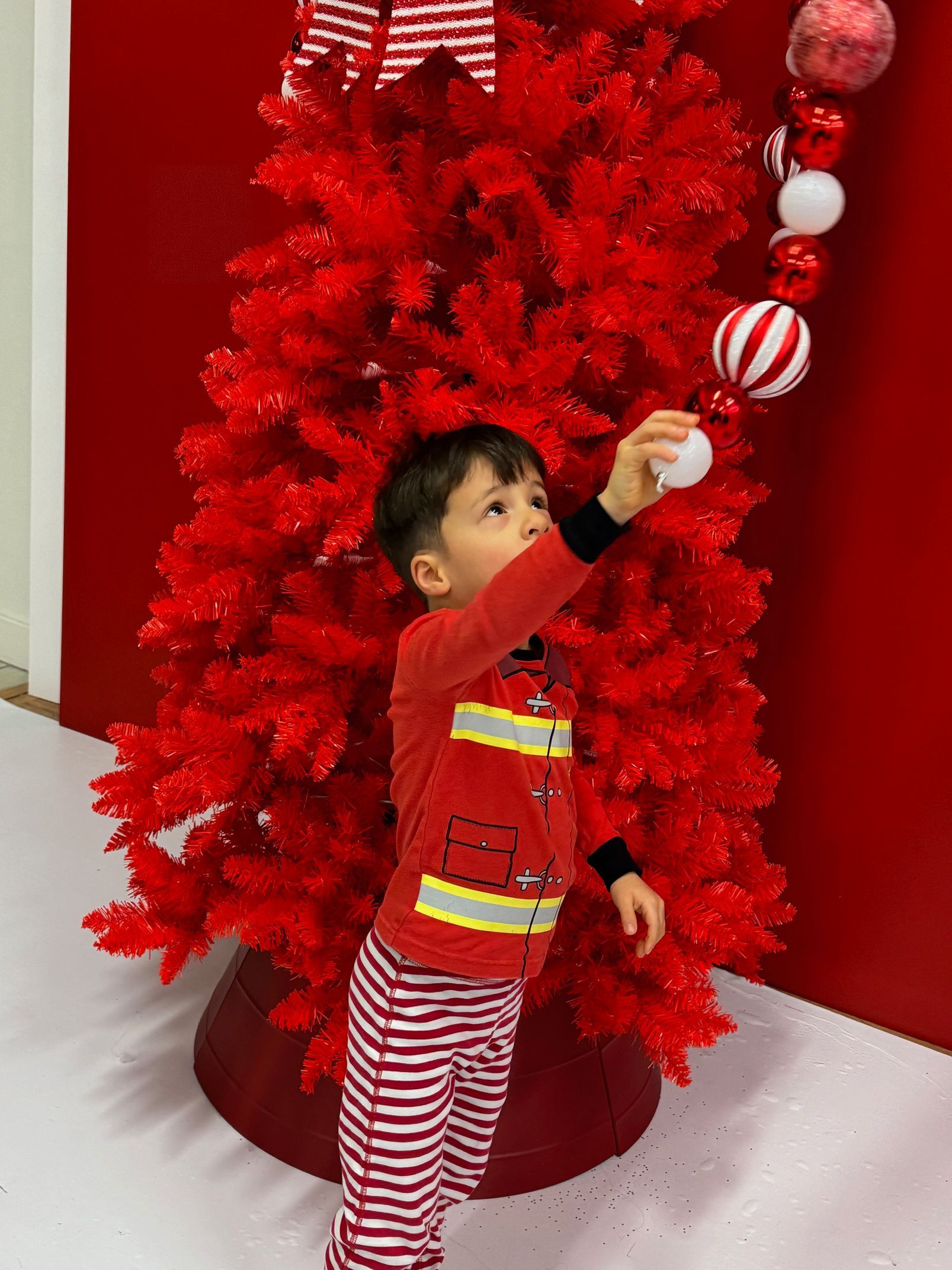 A little boy is decorating a red christmas tree
