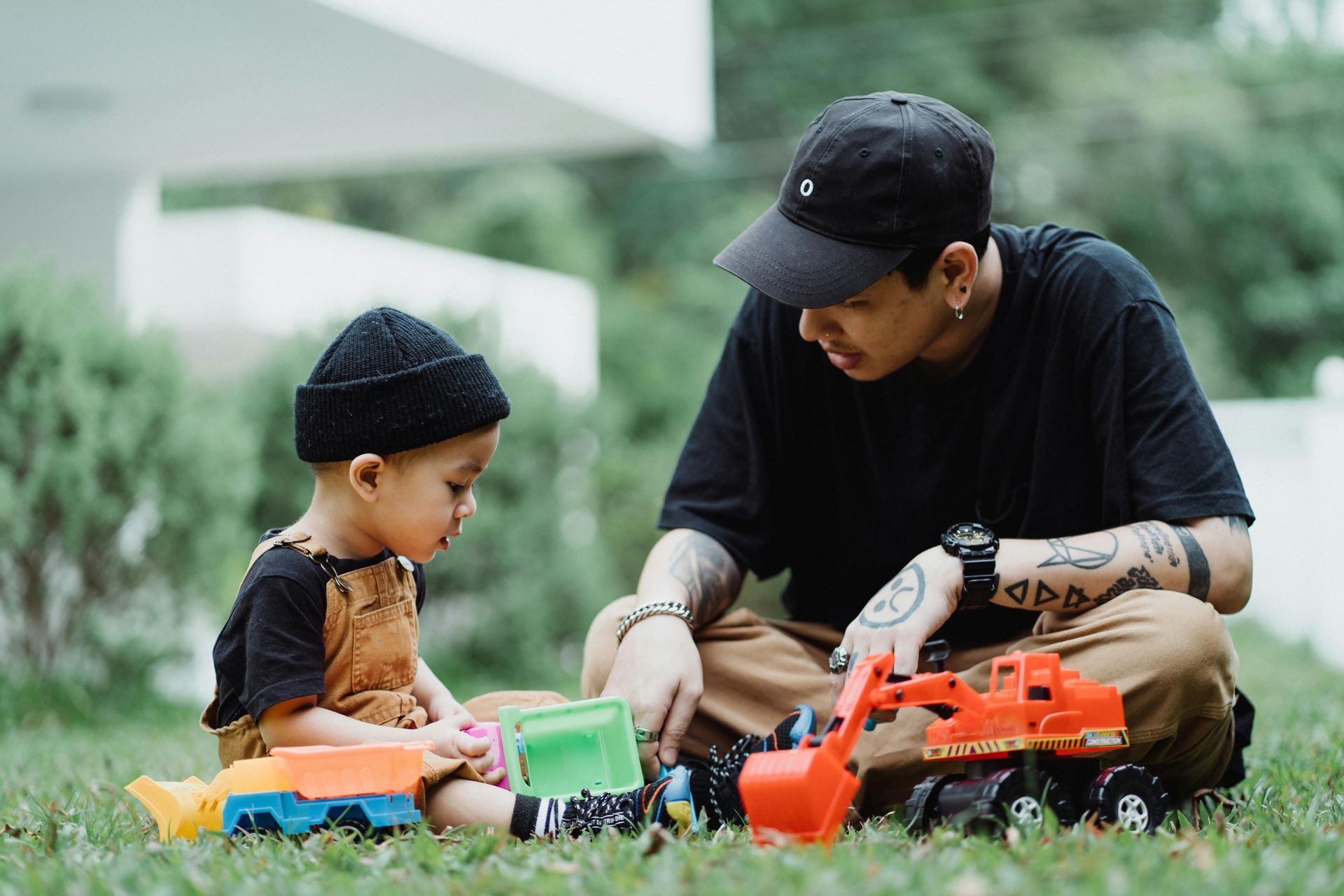 A man and a child are playing with toy trucks in the grass.