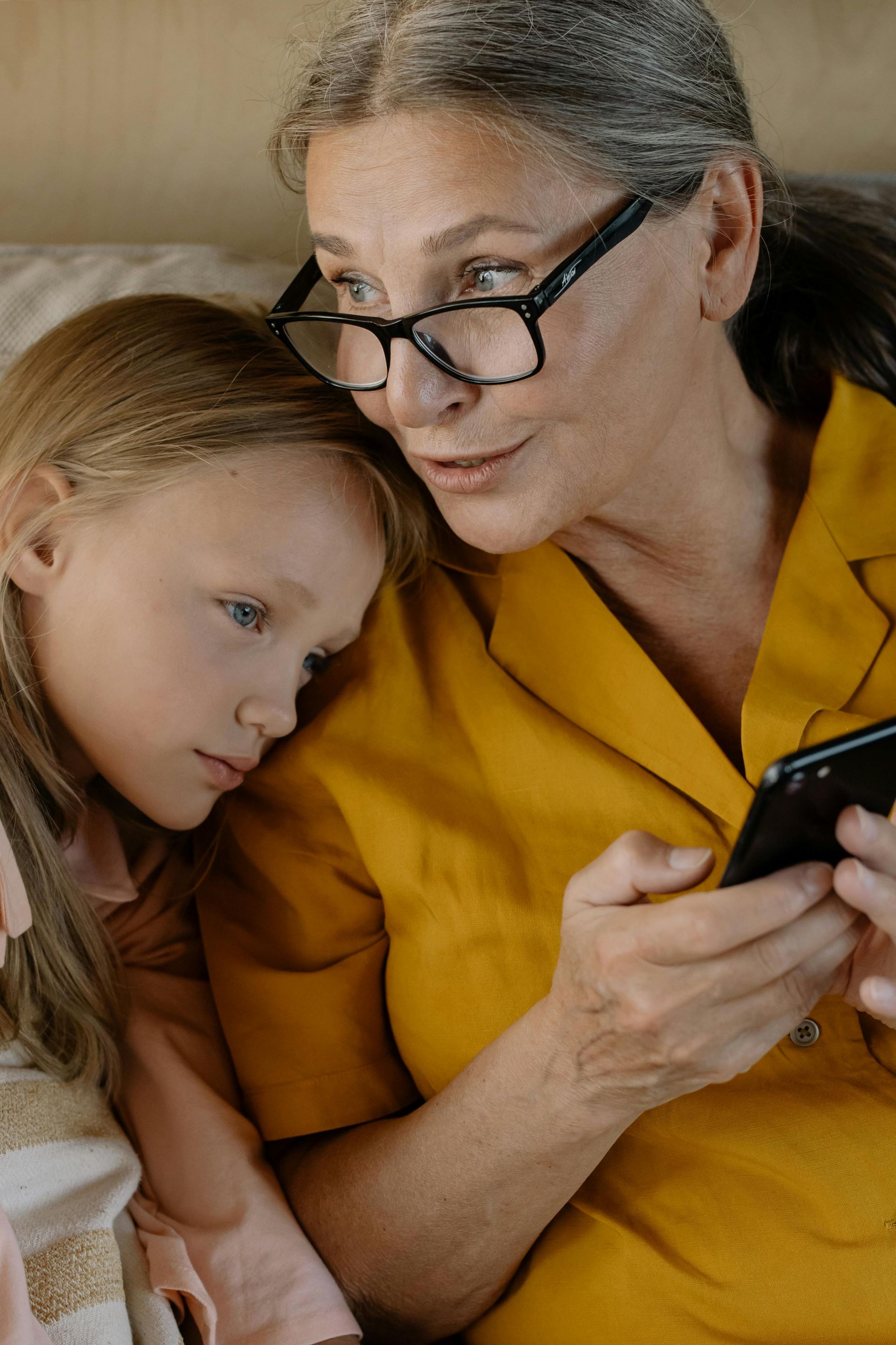 A woman and a little girl are looking at a cell phone.