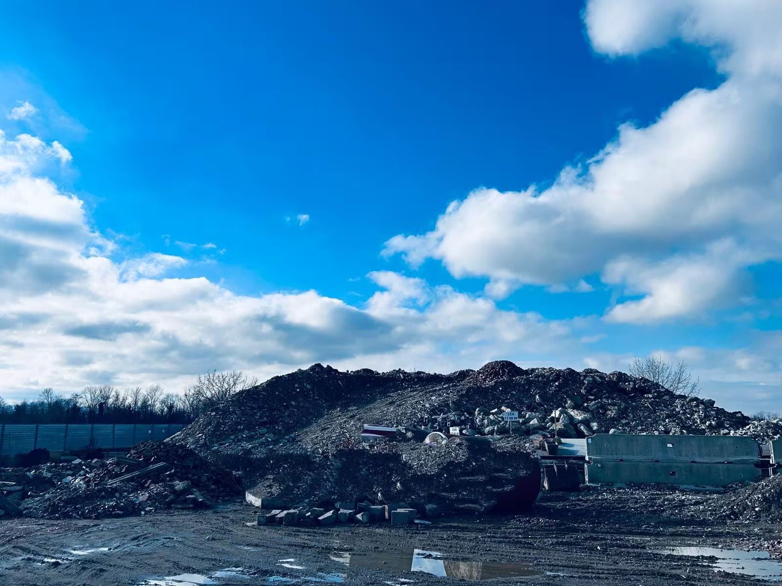 Un cumulo di detriti sotto un cielo azzurro e parzialmente nuvoloso. Barriere di cemento delimitano i lati sinistro e destro.