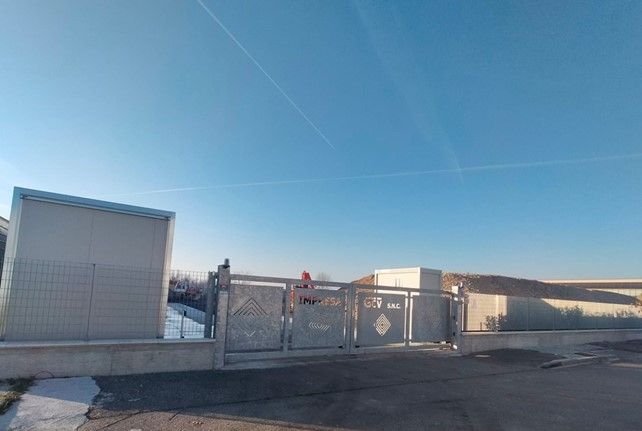 Cancello metallico e edificio in una giornata limpida e soleggiata.
