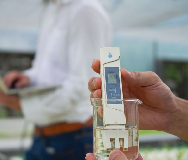 A Person is Holding a Thermometer Over a Glass of Water — Hastings Water Care In Redbank, NSW