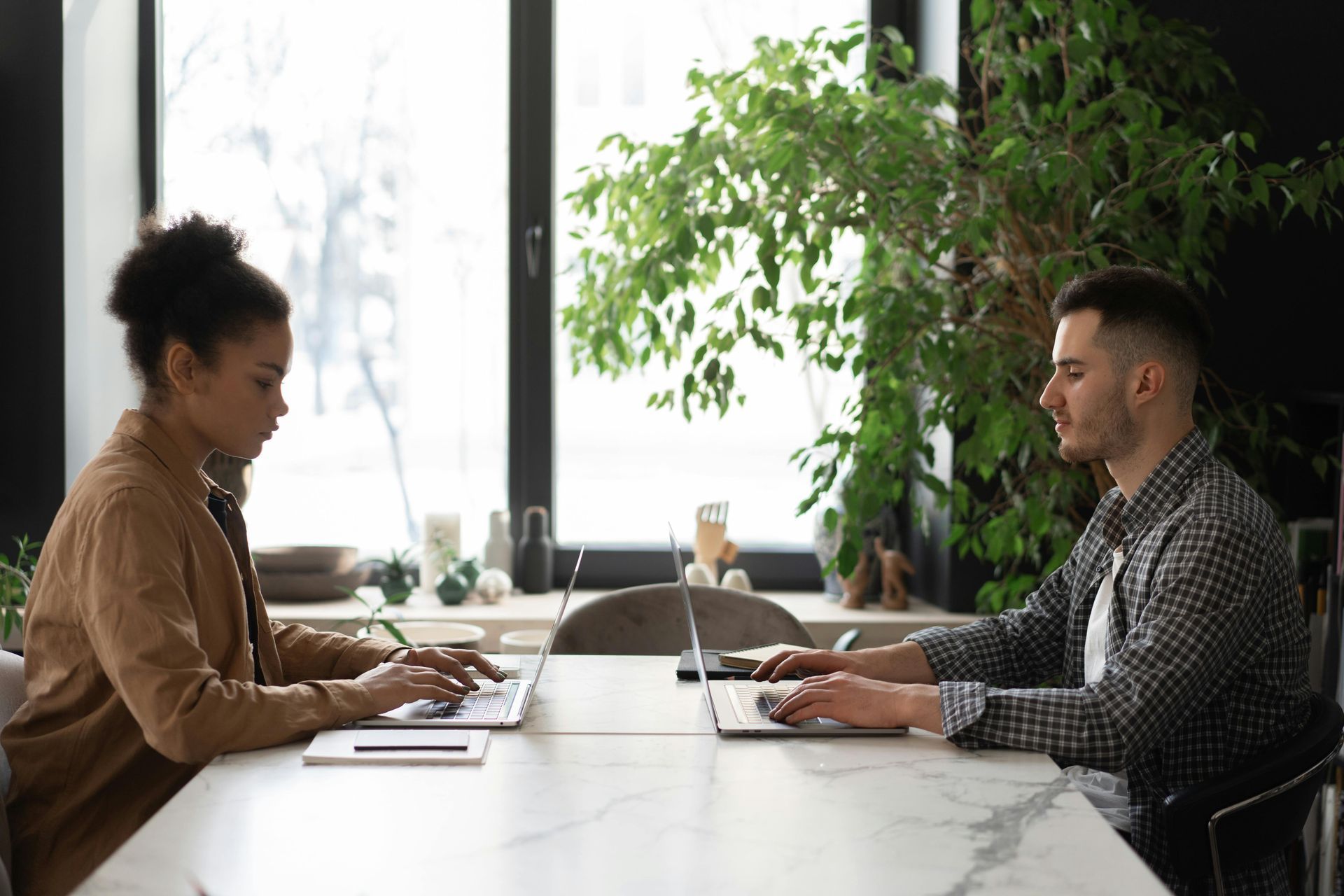 A man and a woman are sitting at a table using laptops.