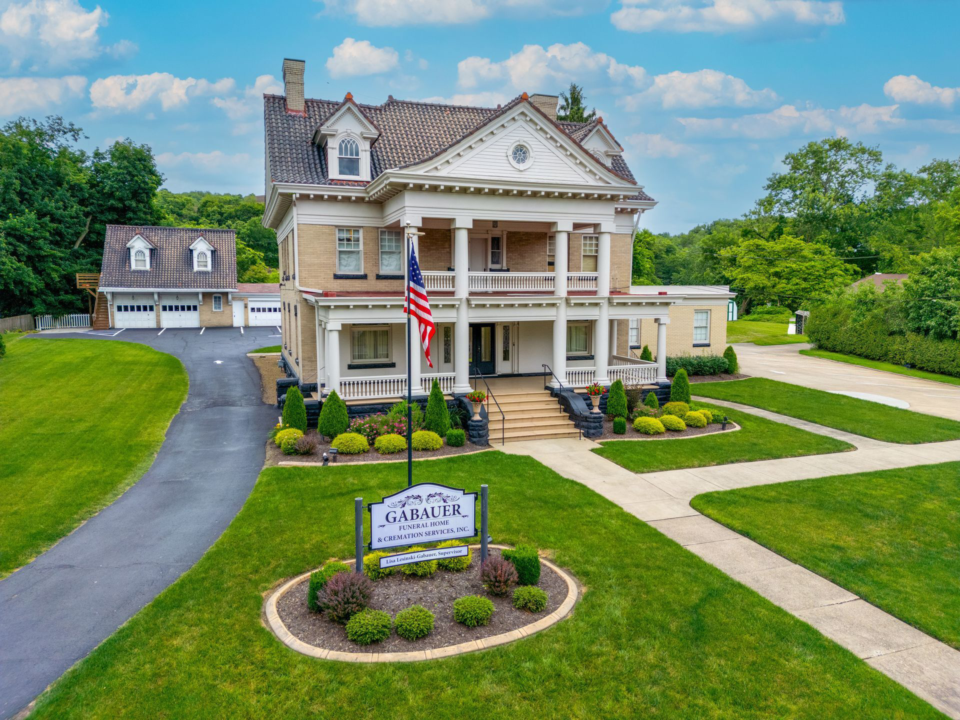 Historic white mansion with columns, American flag, and manicured lawn under a blue sky.