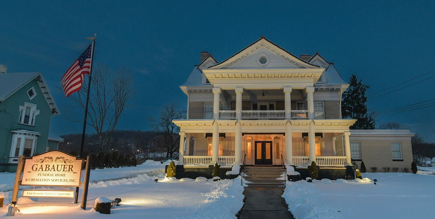 Snowy town hall at dusk with lit columns, an American flag, and a roadside sign.