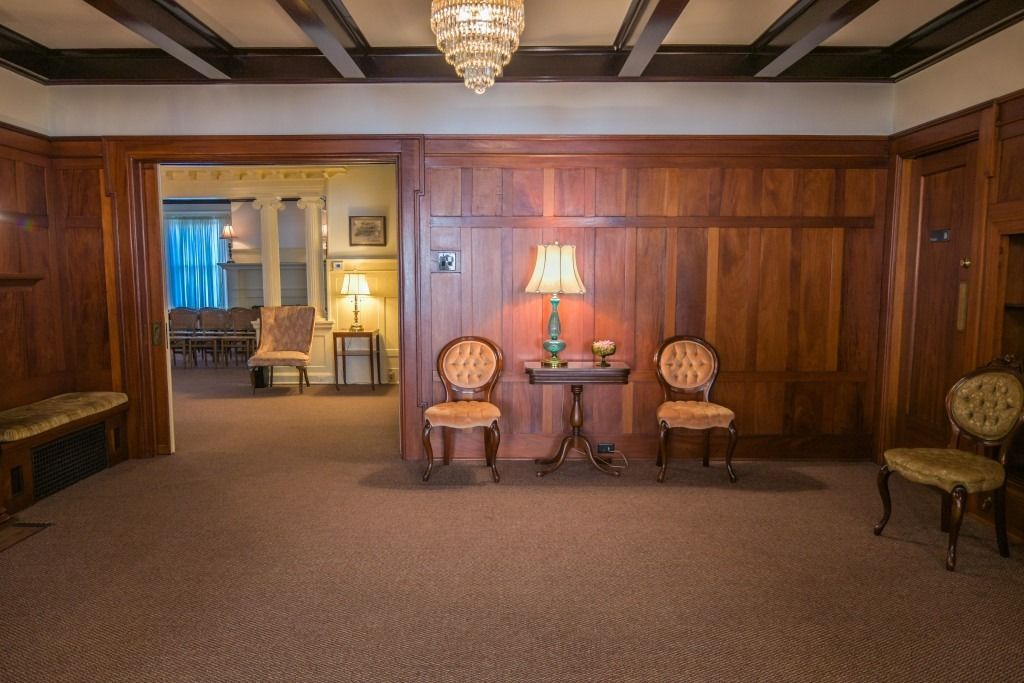 Wood-paneled lounge with patterned chairs, a table lamp, and an open doorway to a dining room