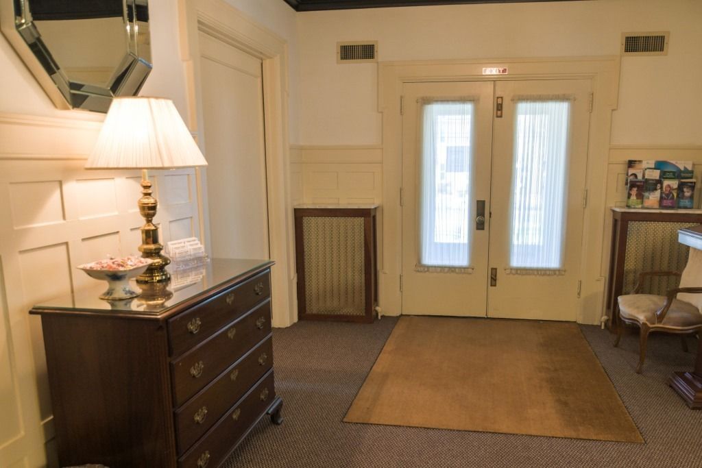 Hallway with a dark wood dresser, lamp, rug, and double front doors with sheer curtains