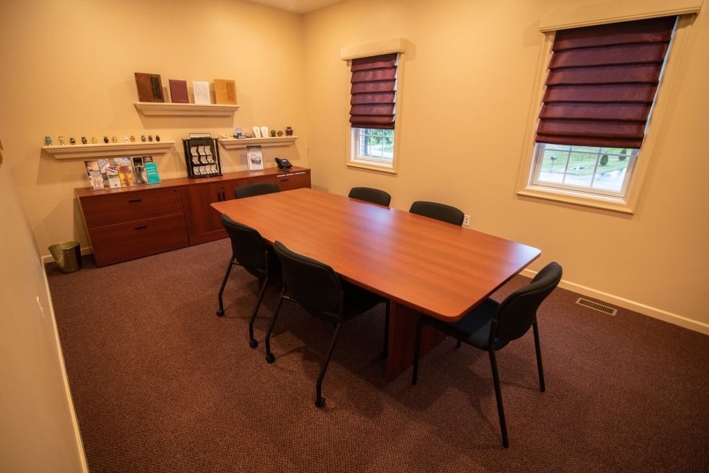 Conference room with wooden table, black chairs, and burgundy blinds on two windows.