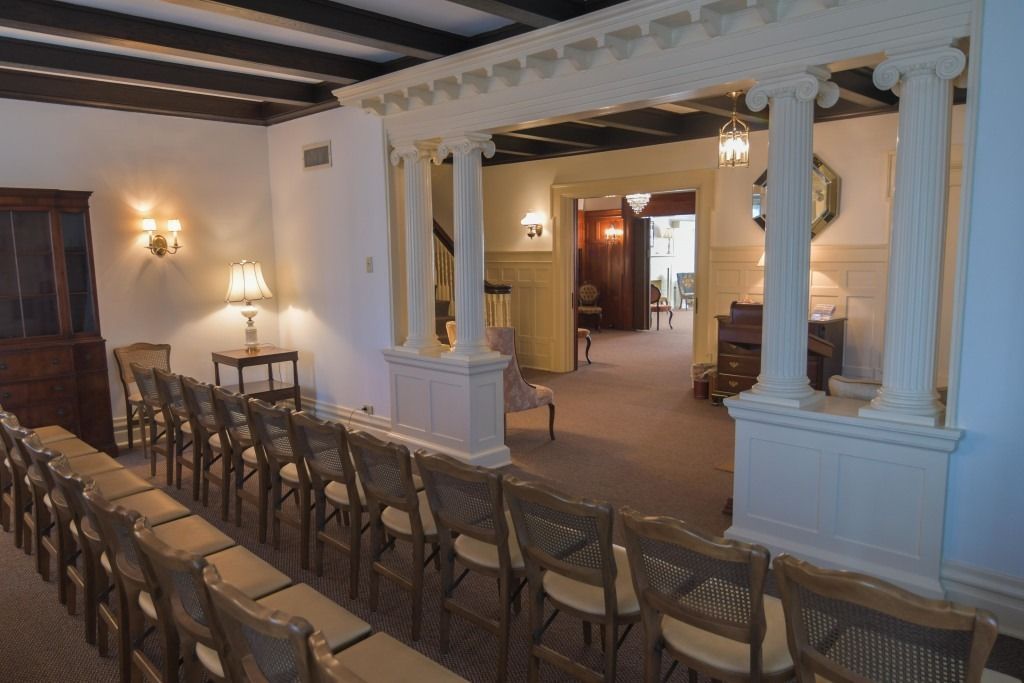 Elegant hall with rows of chairs facing a white columned stage and warm wall sconces