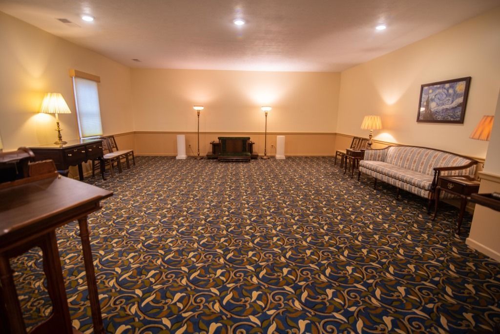 Empty banquet hall with patterned carpet, beige walls, framed art, tables, and warm lamps along the sides