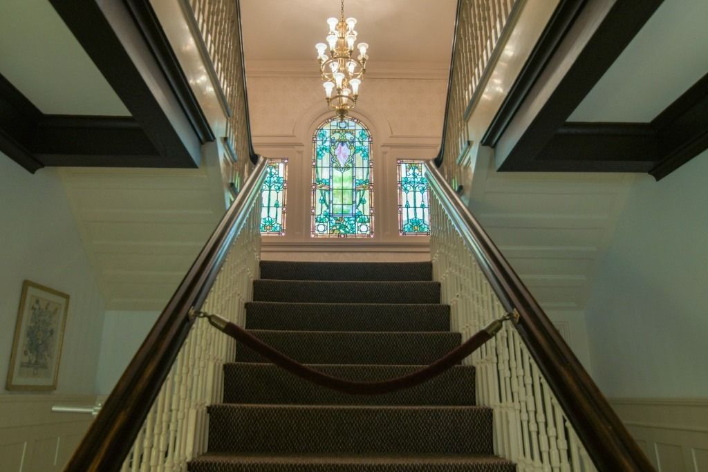 Grand staircase in a mansion with chandelier and stained-glass windows at the top
