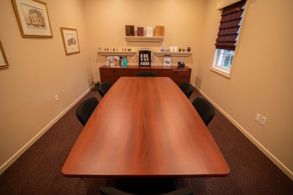 Conference room with a long wooden table, black chairs, and a sideboard against beige walls.