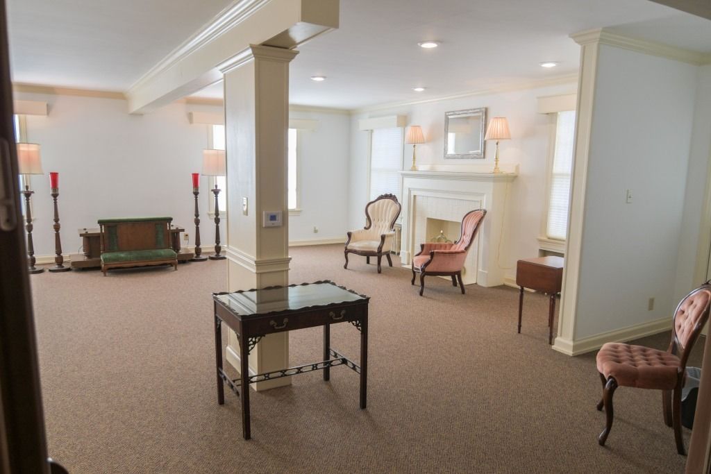 Bright, empty living room with beige carpet, white columns, and assorted armchairs near a fireplace.