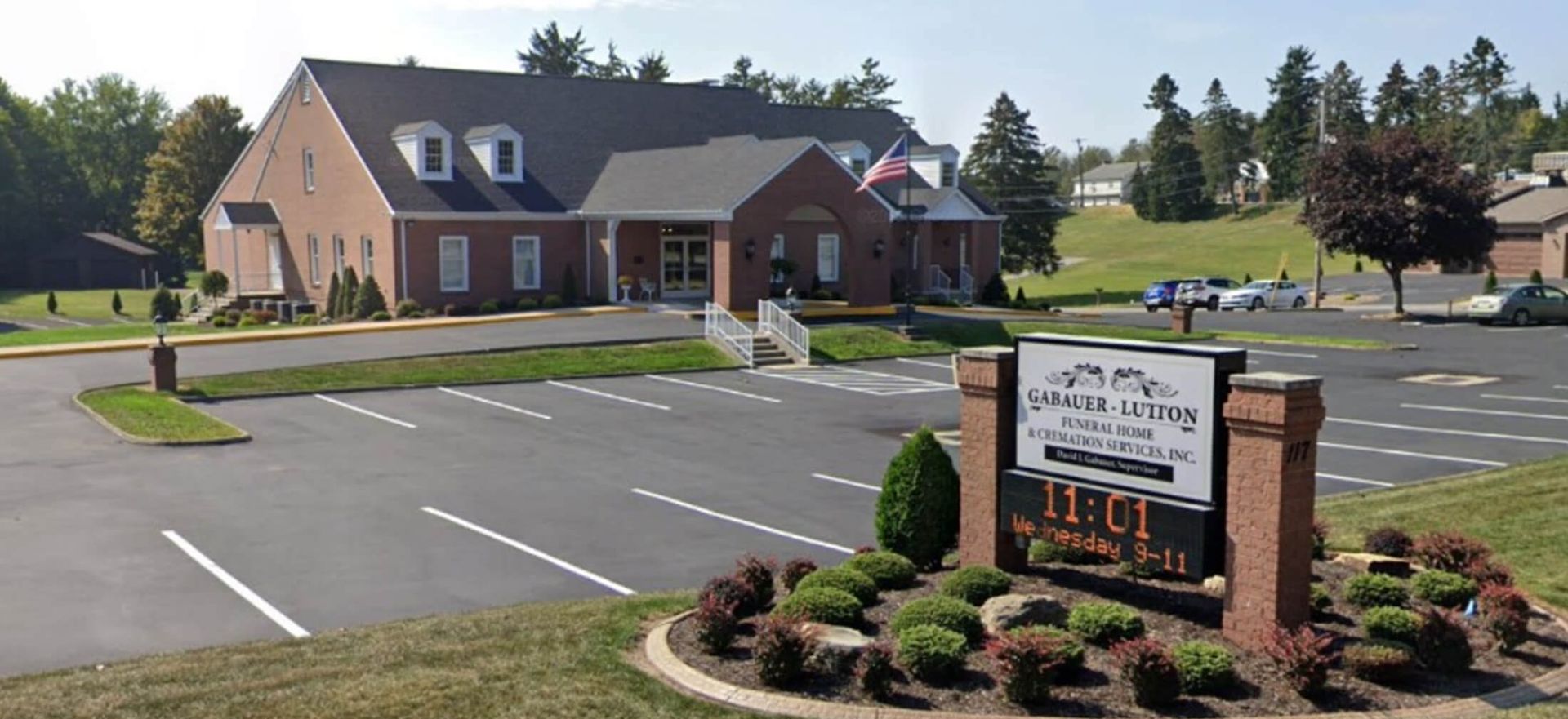 Brick office building with parking lot and roadside sign in a landscaped suburban setting