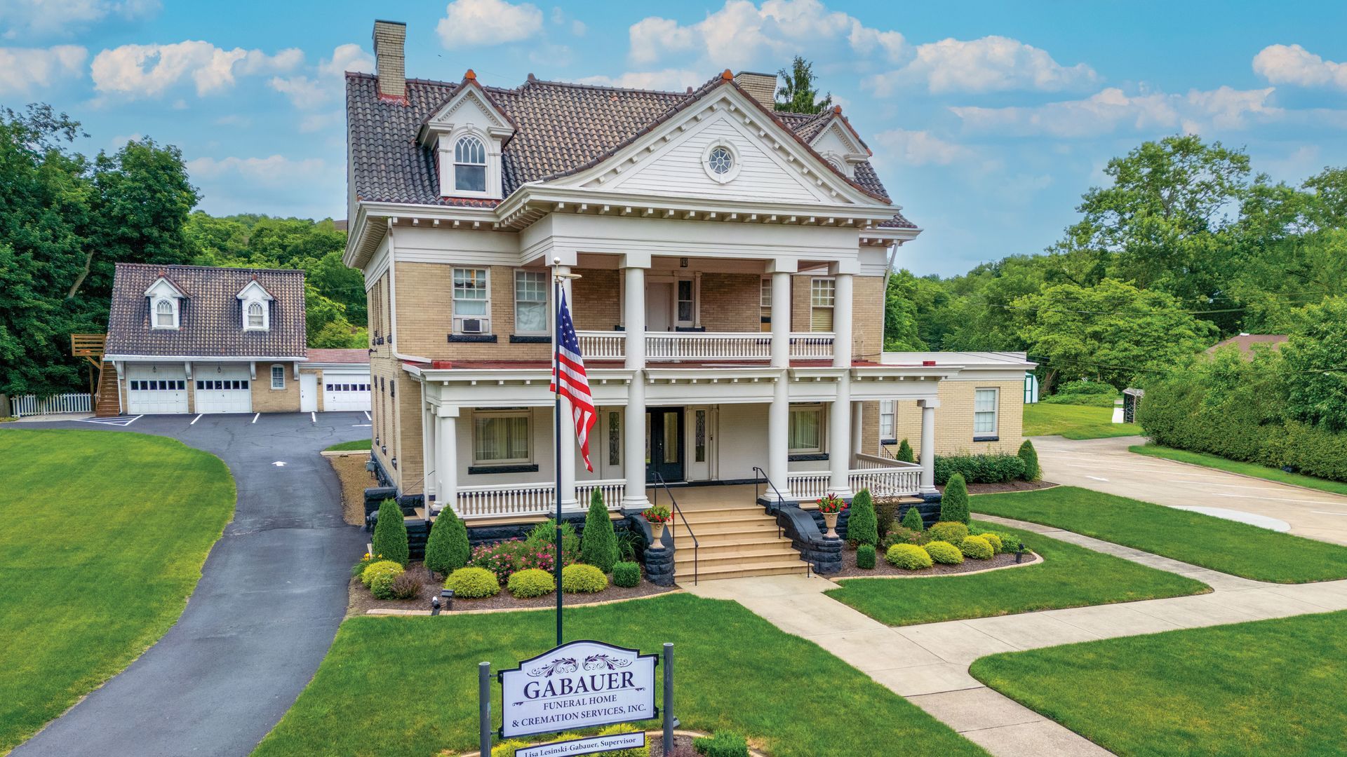 Historic white mansion with columns, American flag, and manicured lawn under a blue sky.