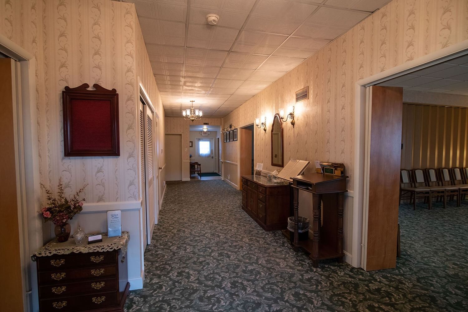Empty hotel hallway with patterned carpet, wood-paneled walls, and wall sconces