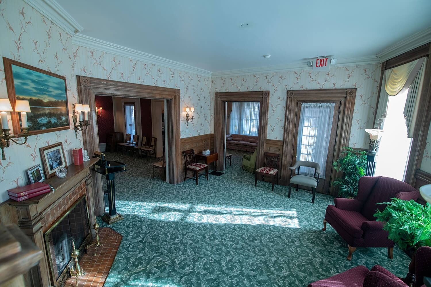 Bright lobby with floral wallpaper, green carpet, fireplace, chairs, and sunlight through windows