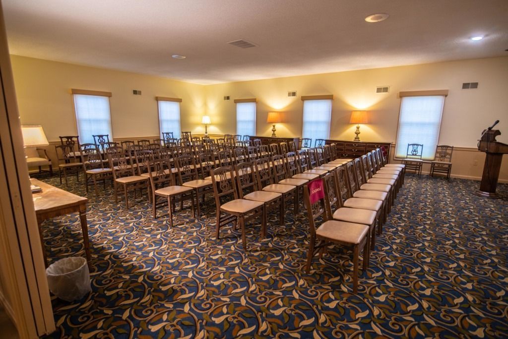 Empty banquet hall with rows of long tables and chairs on a patterned carpet, lit by warm ceiling lights