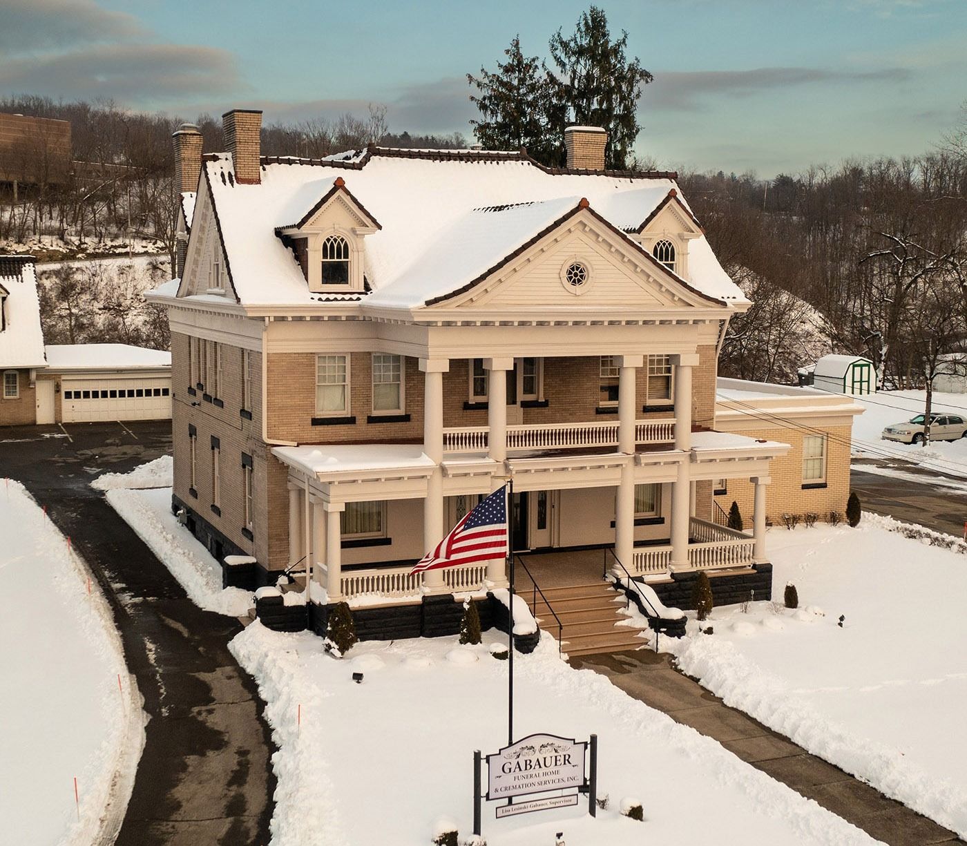 Snowy historic house with American flag and porch in winter landscape