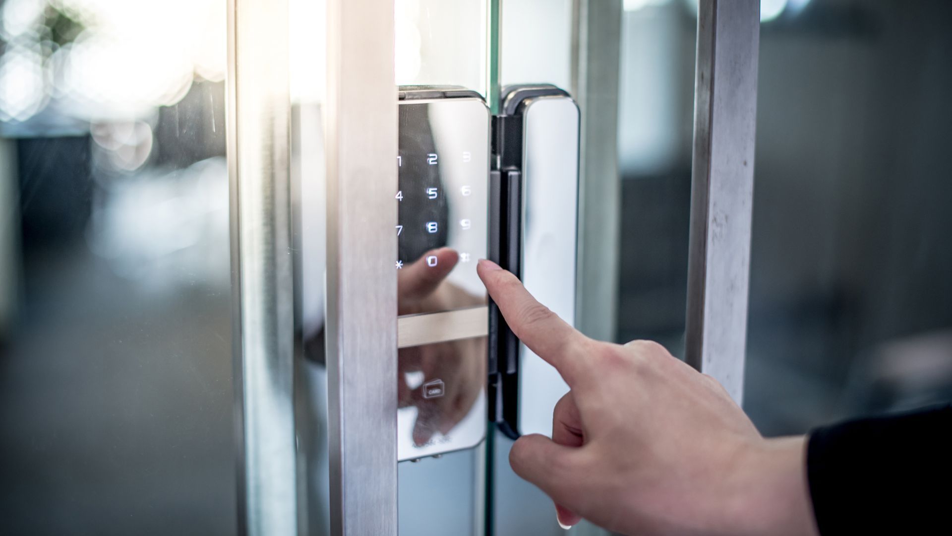 Finger pressing a silver door access button on a glass door