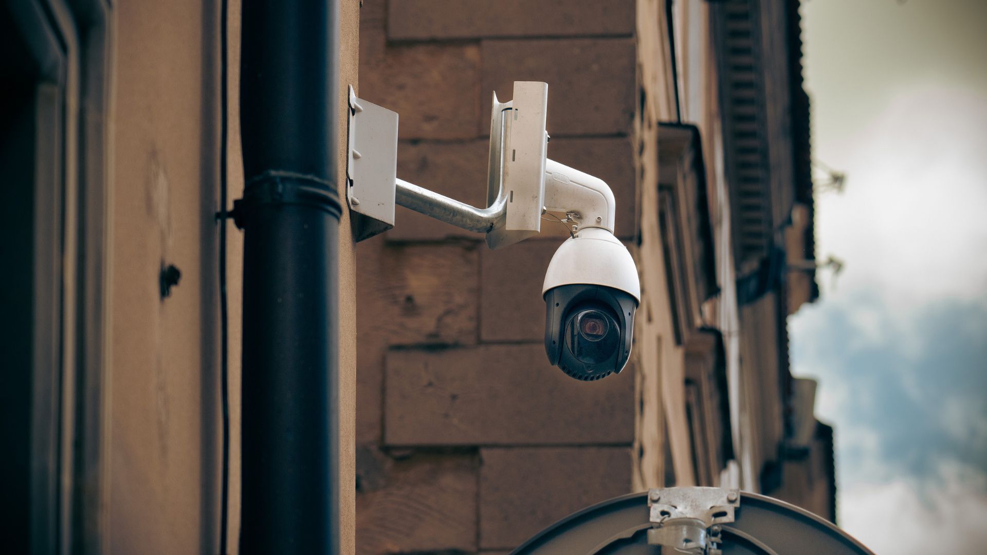White security camera mounted on a building wall, overlooking a narrow alleyway.