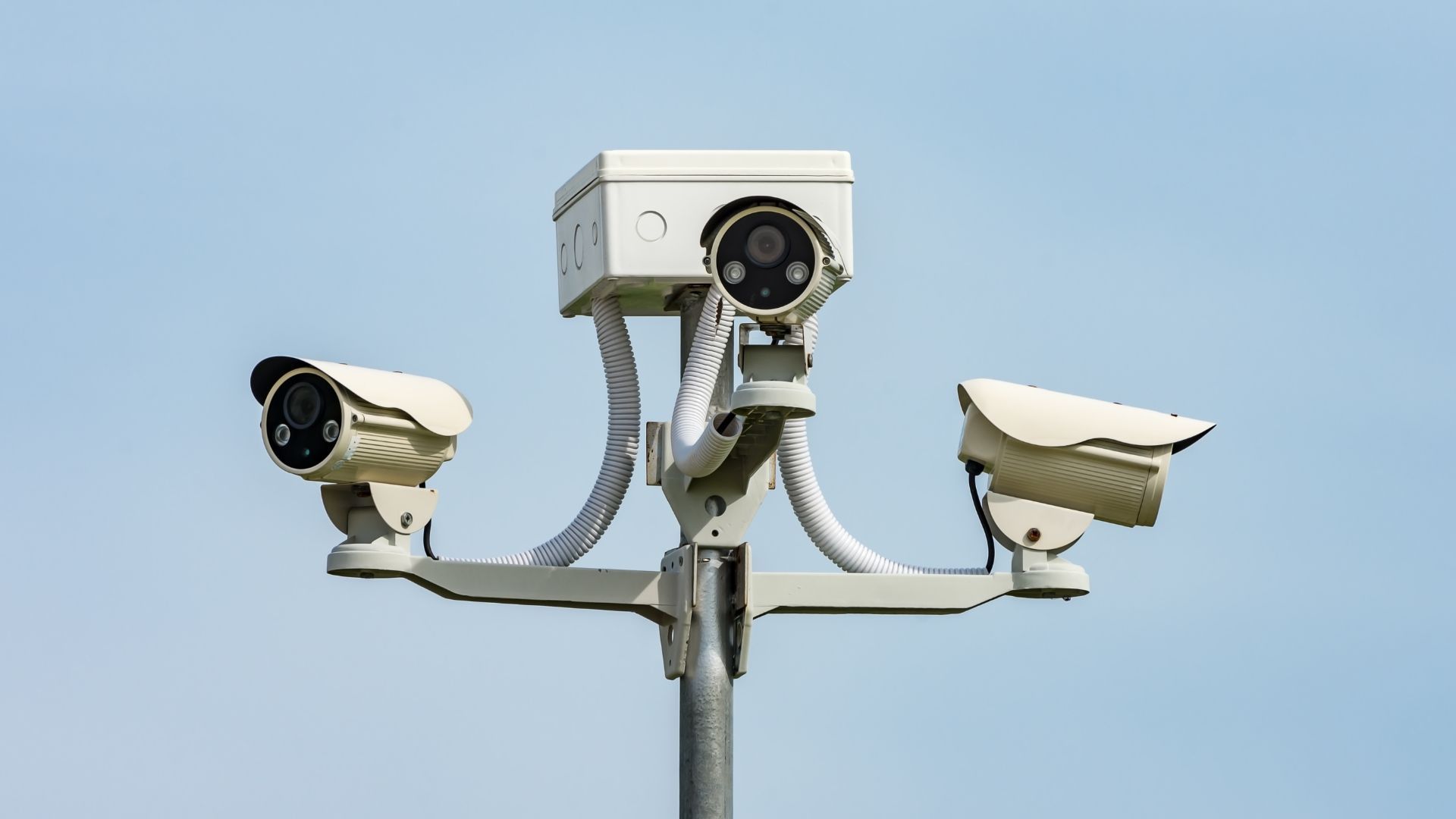 Three security cameras mounted on a pole against a blue sky