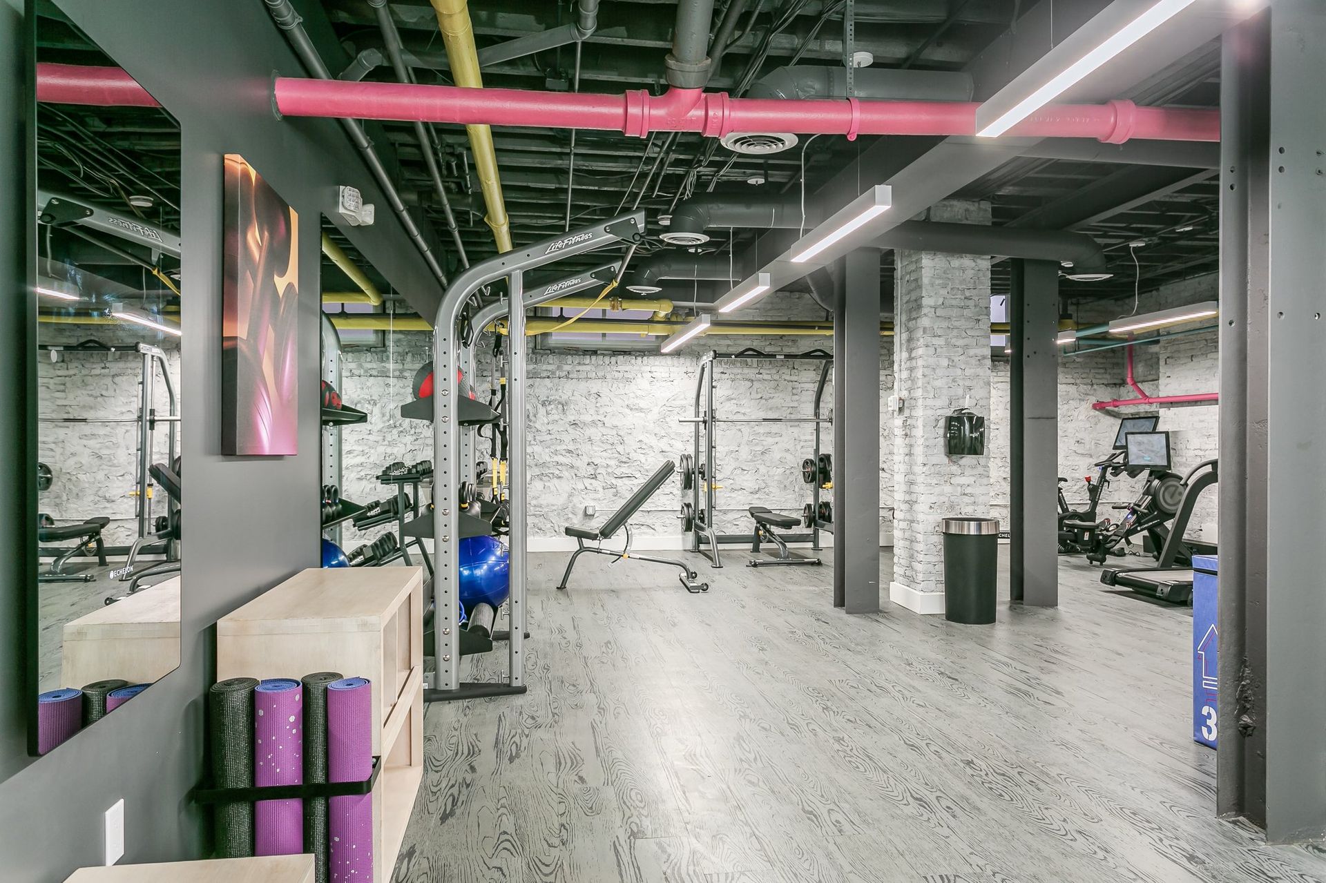 Image of the fitness center at the Normandie apartments, showing free weights, smith machine, yoga mats
