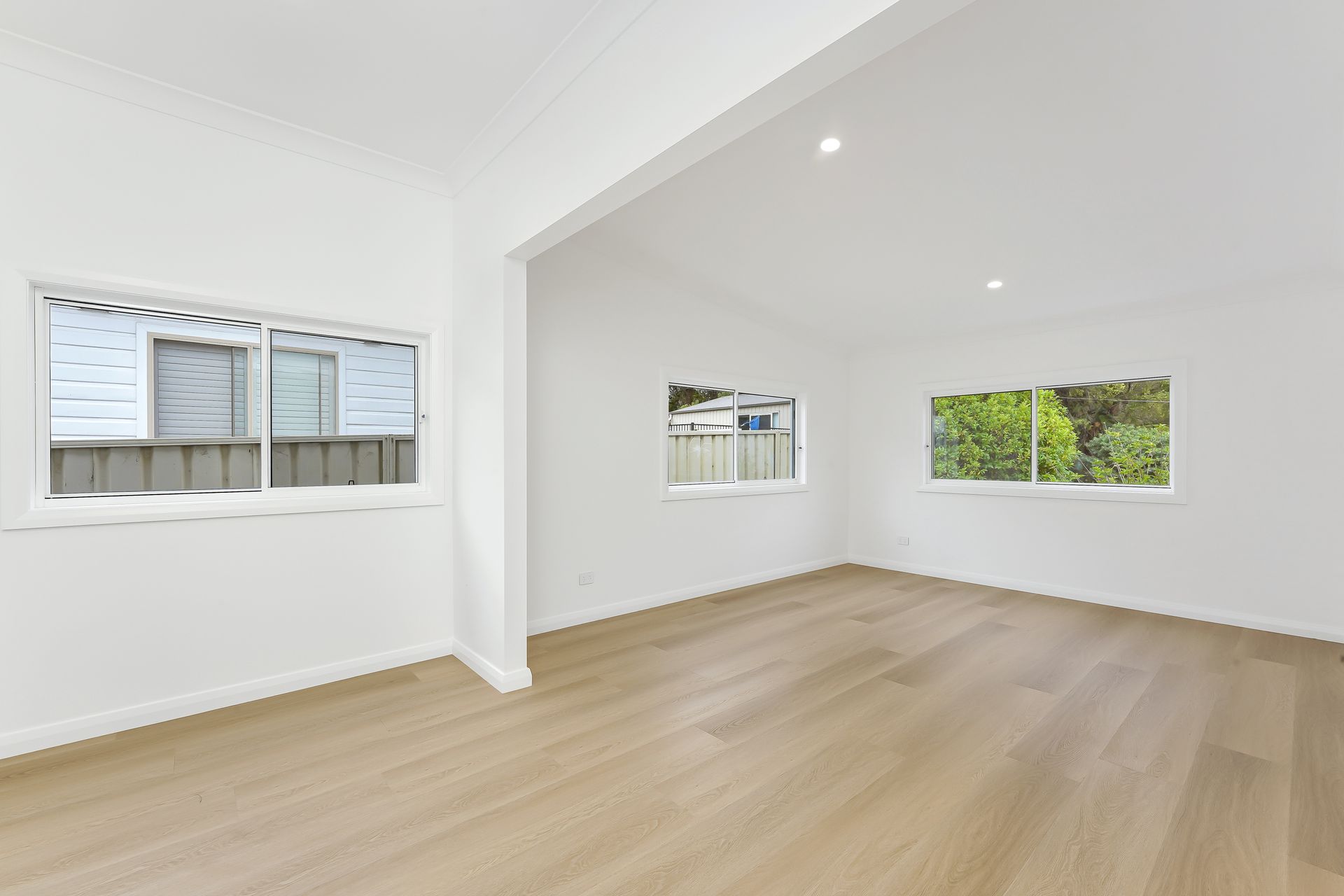 Empty, bright room with light wood floors, white walls, and three windows.