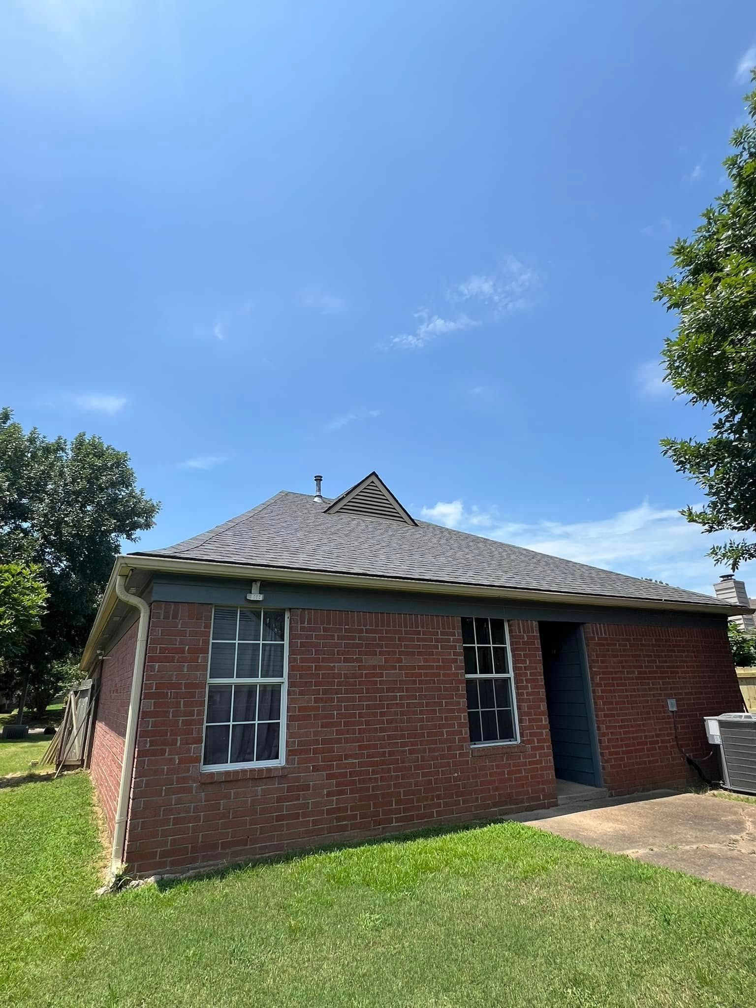 Small red brick house with a gray roof, blue door, and windows under a bright blue sky.