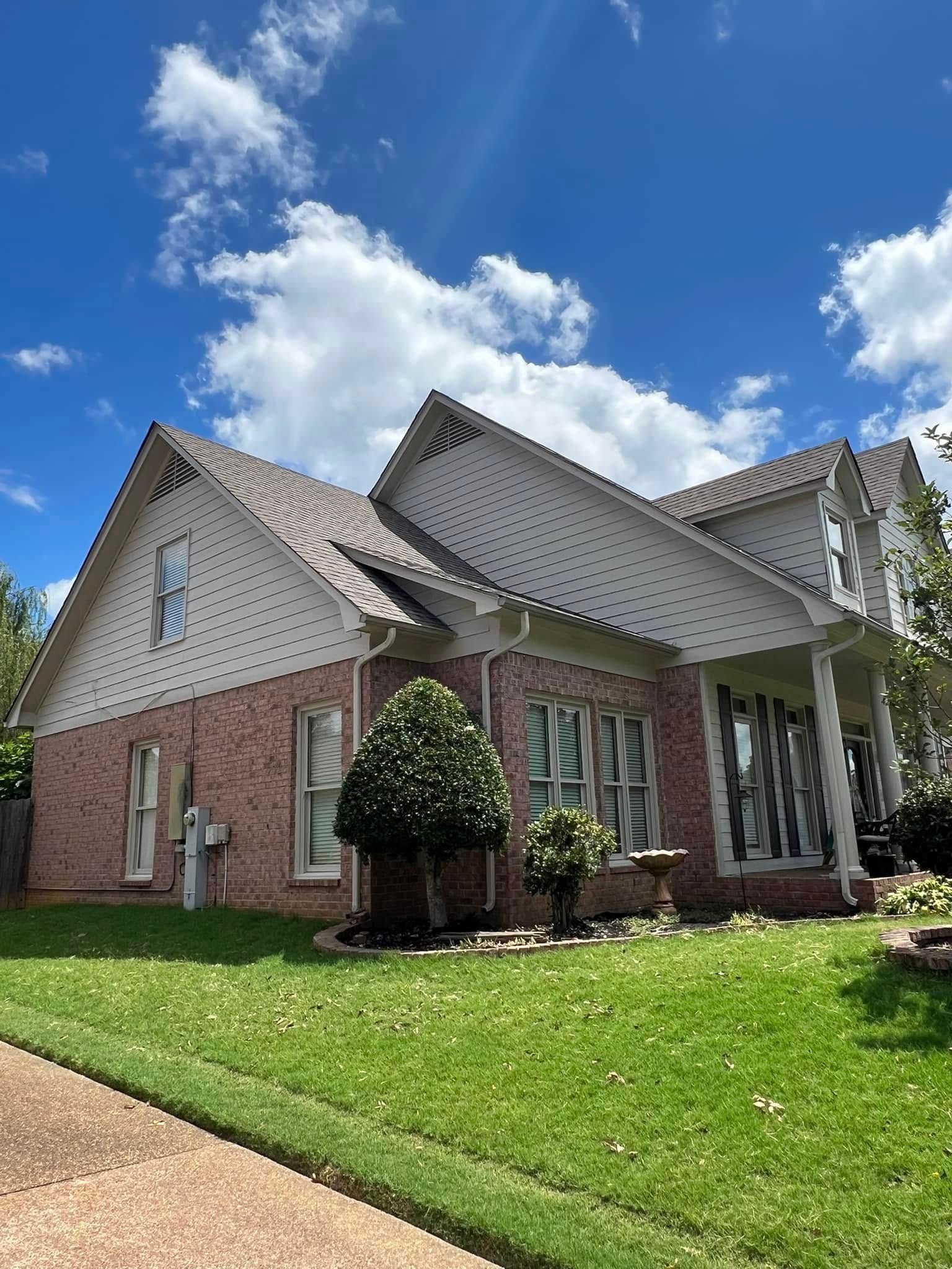 Brick house with white gables and a front porch on a green lawn under a blue sky