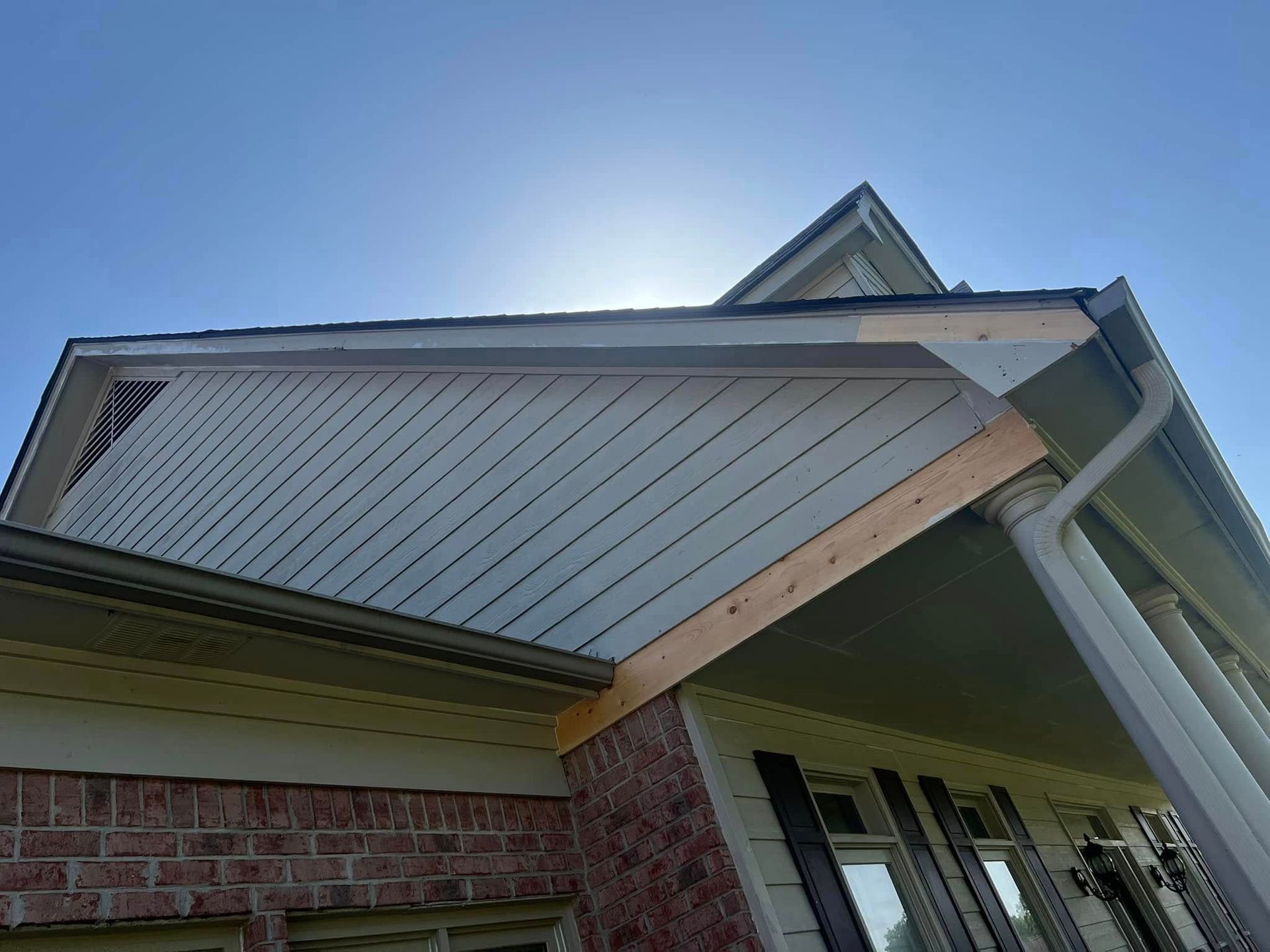 Front of a brick house with a gray gabled roof and white trim against a blue sky