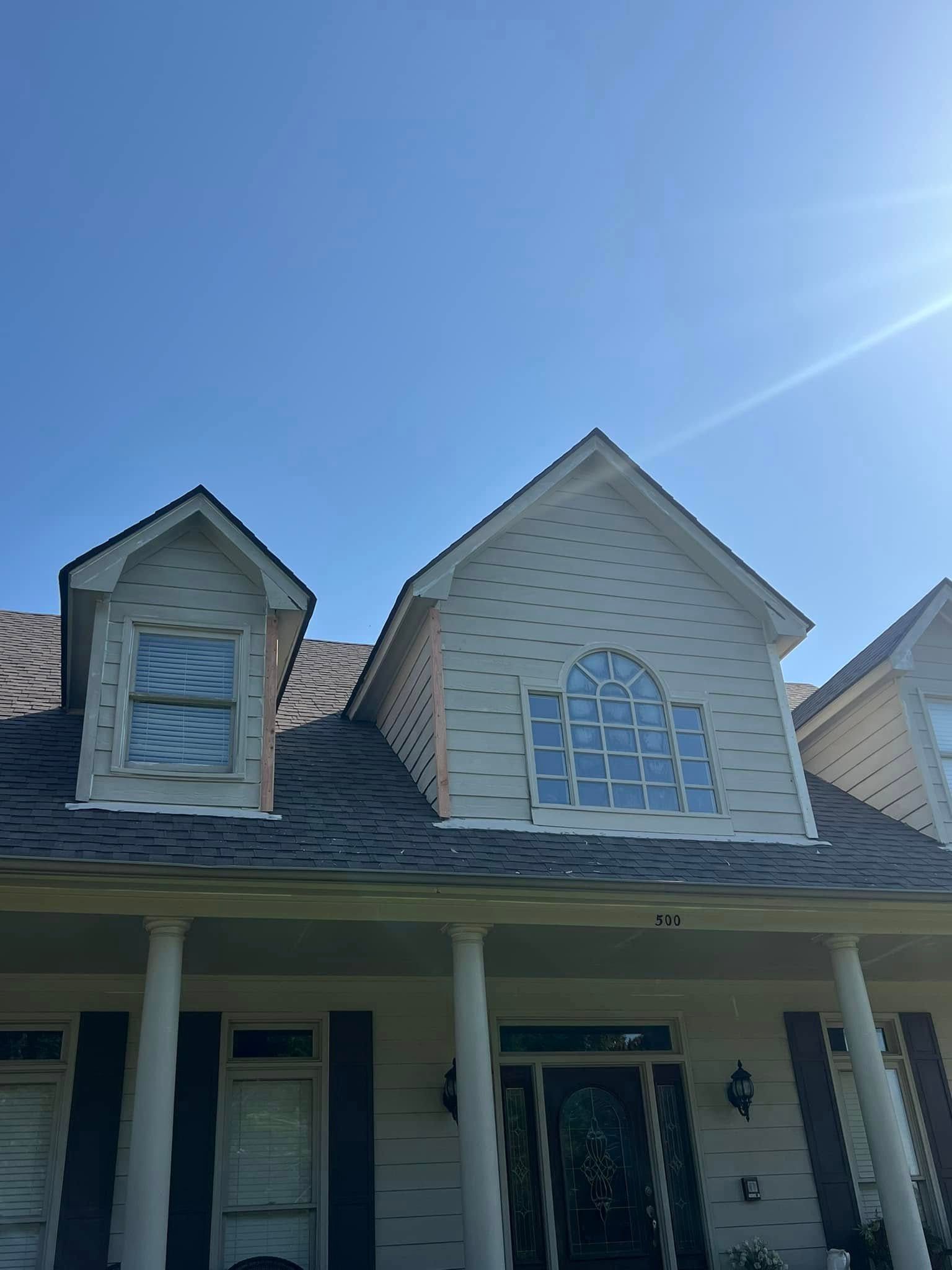 Suburban house exterior with dormer windows, white siding, and a front porch under a blue sky