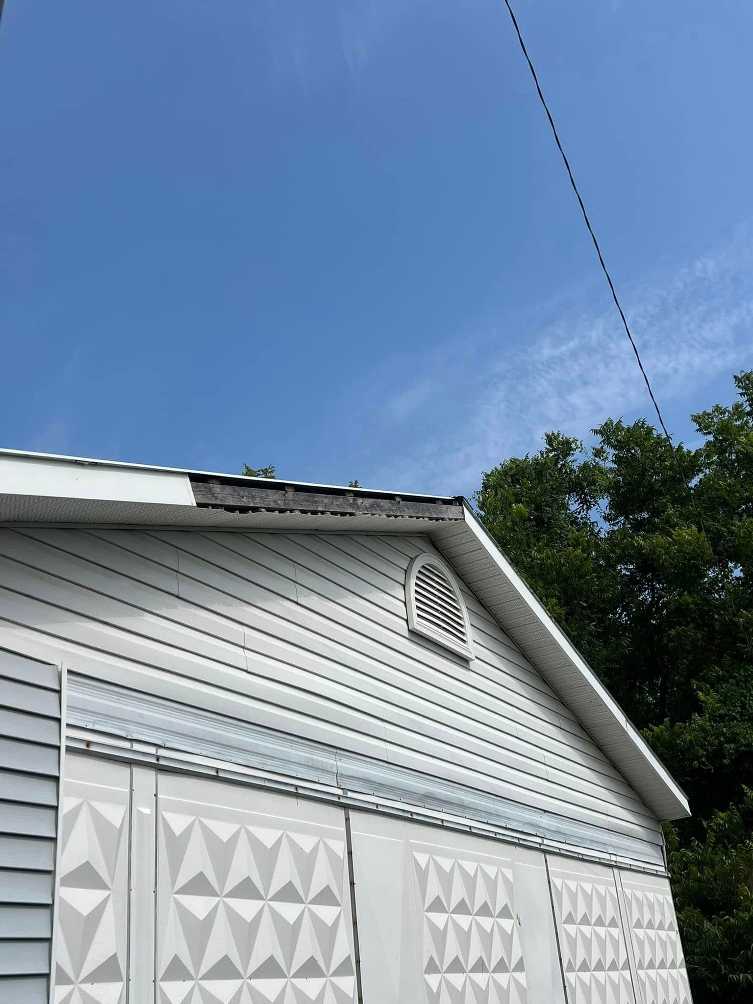 White house siding and roofline with triangular vent against a blue sky, seen from below
