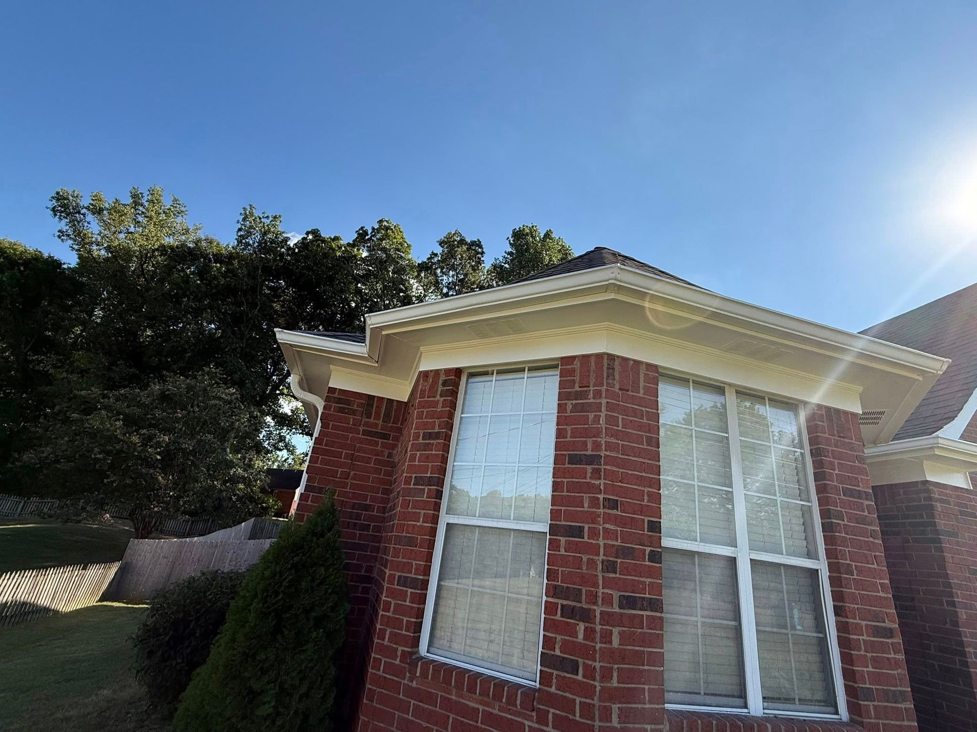 Brick house corner with white-trimmed windows under a bright blue sky