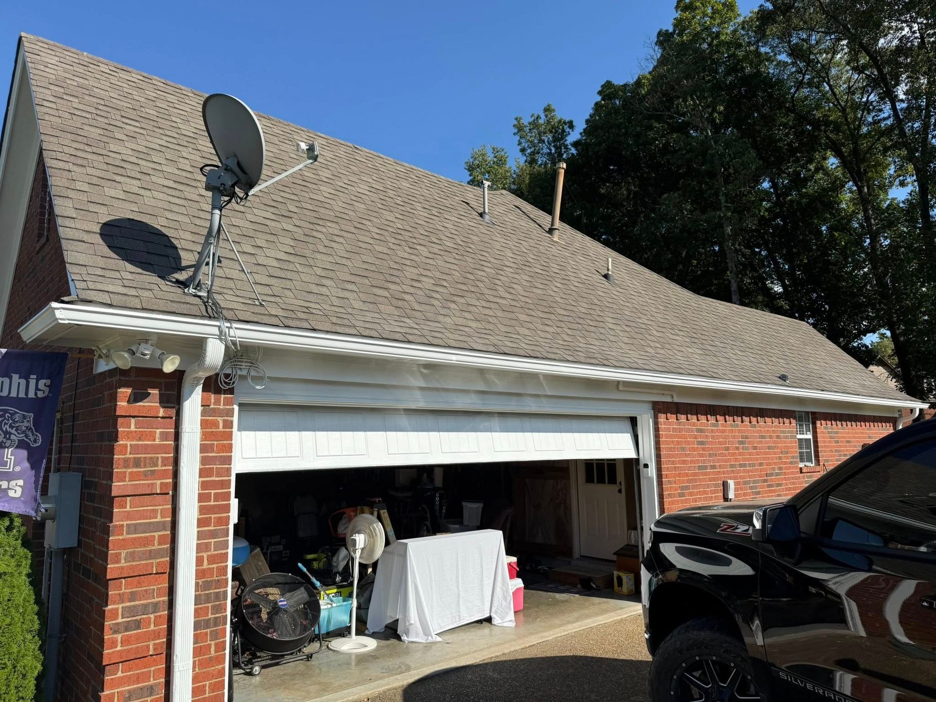 Brick house garage with open door, covered items inside, and a black vehicle parked beside it