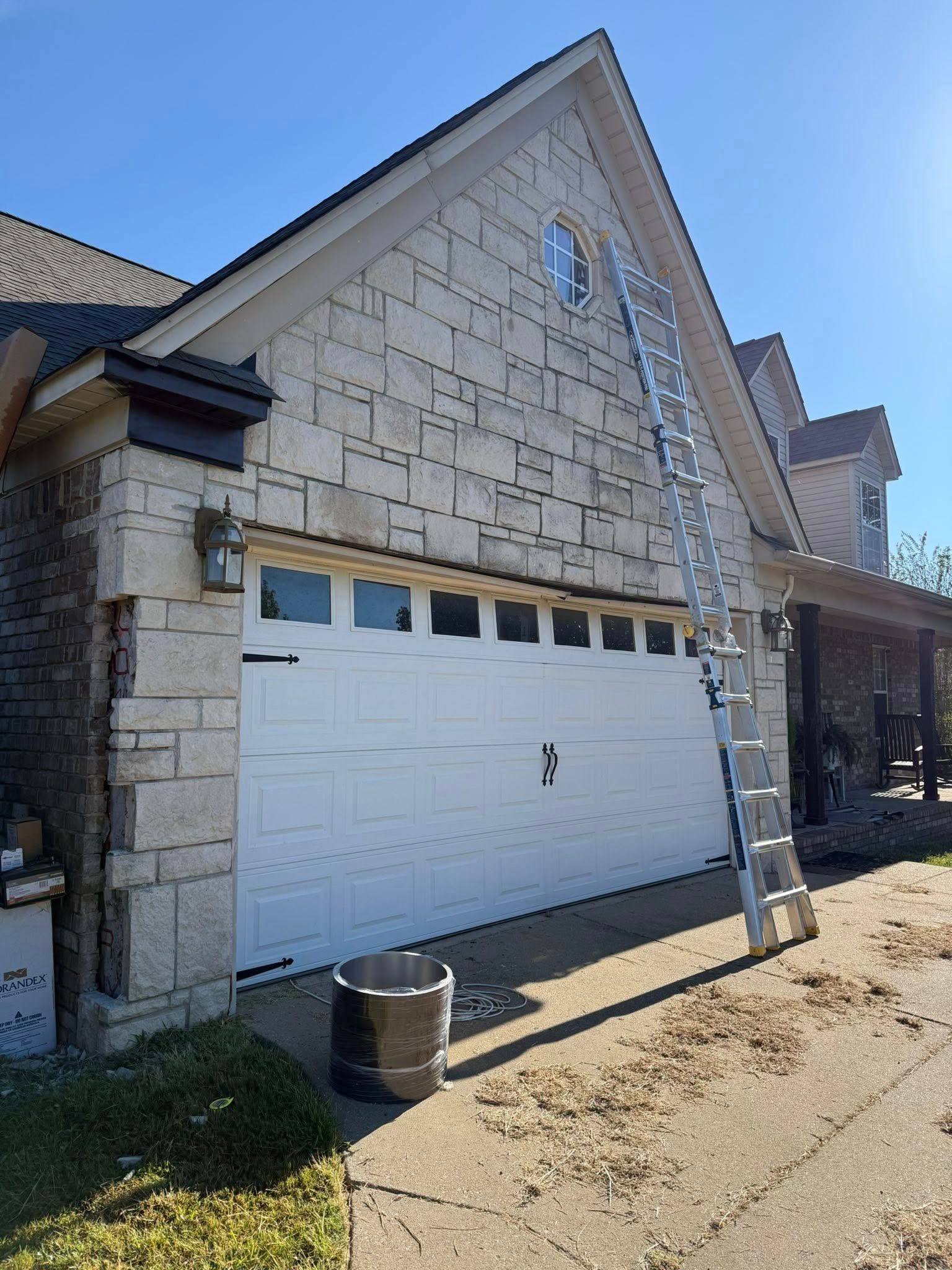 Stone-faced suburban house with a white garage door and front porch in bright sunlight