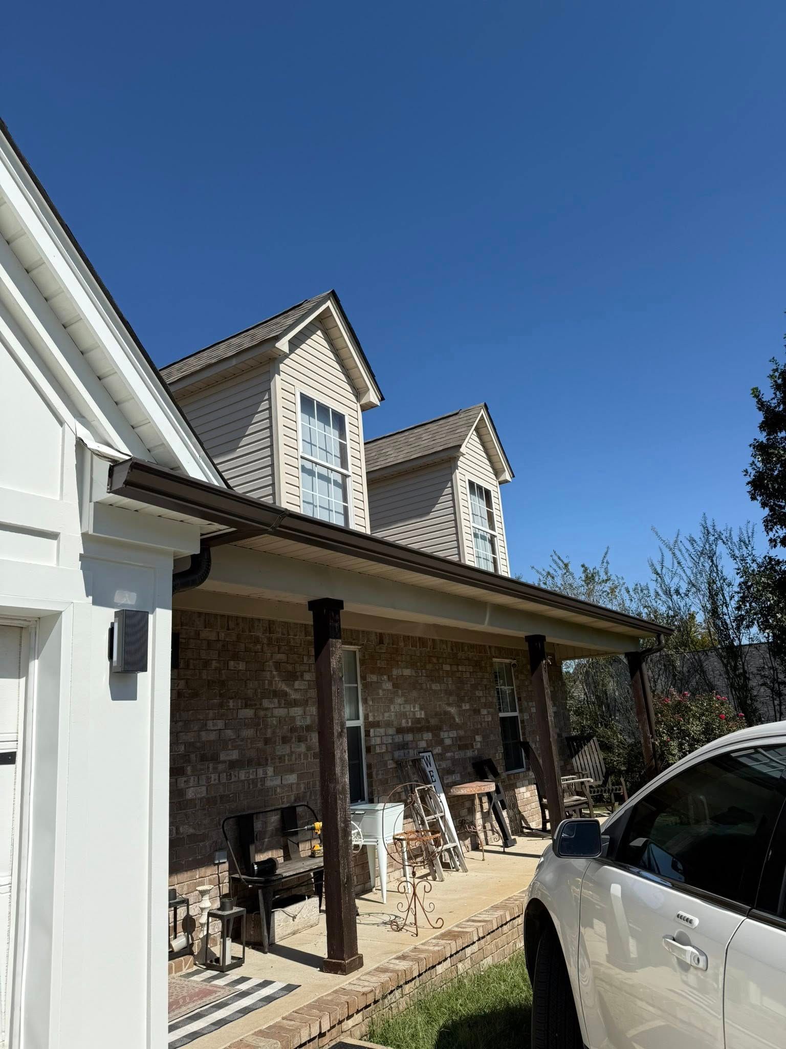 Suburban brick house with covered porch, white siding, and parked white SUV under a clear blue sky
