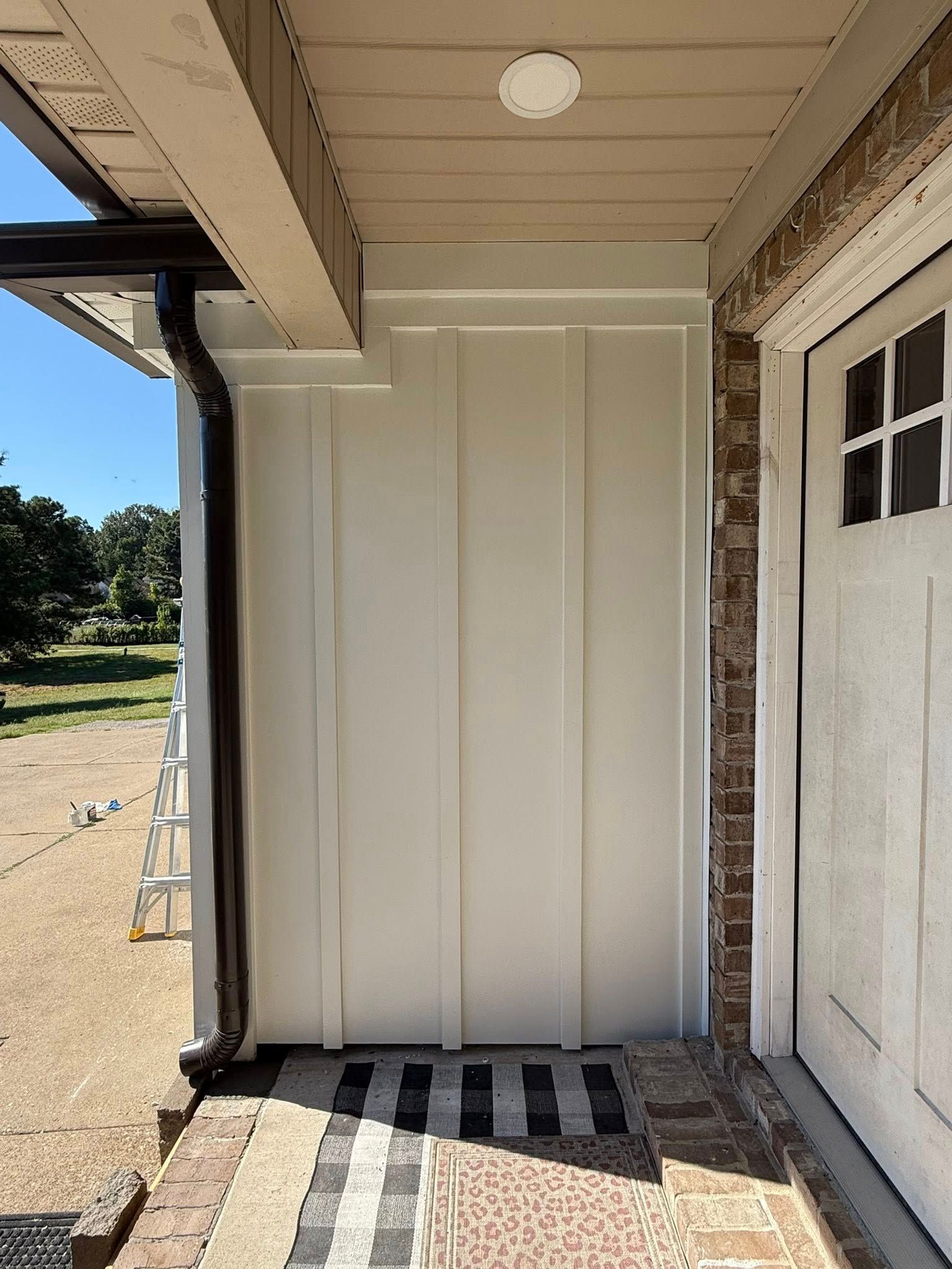 Covered porch with a cream storage cabinet beside a white door and striped doormat.