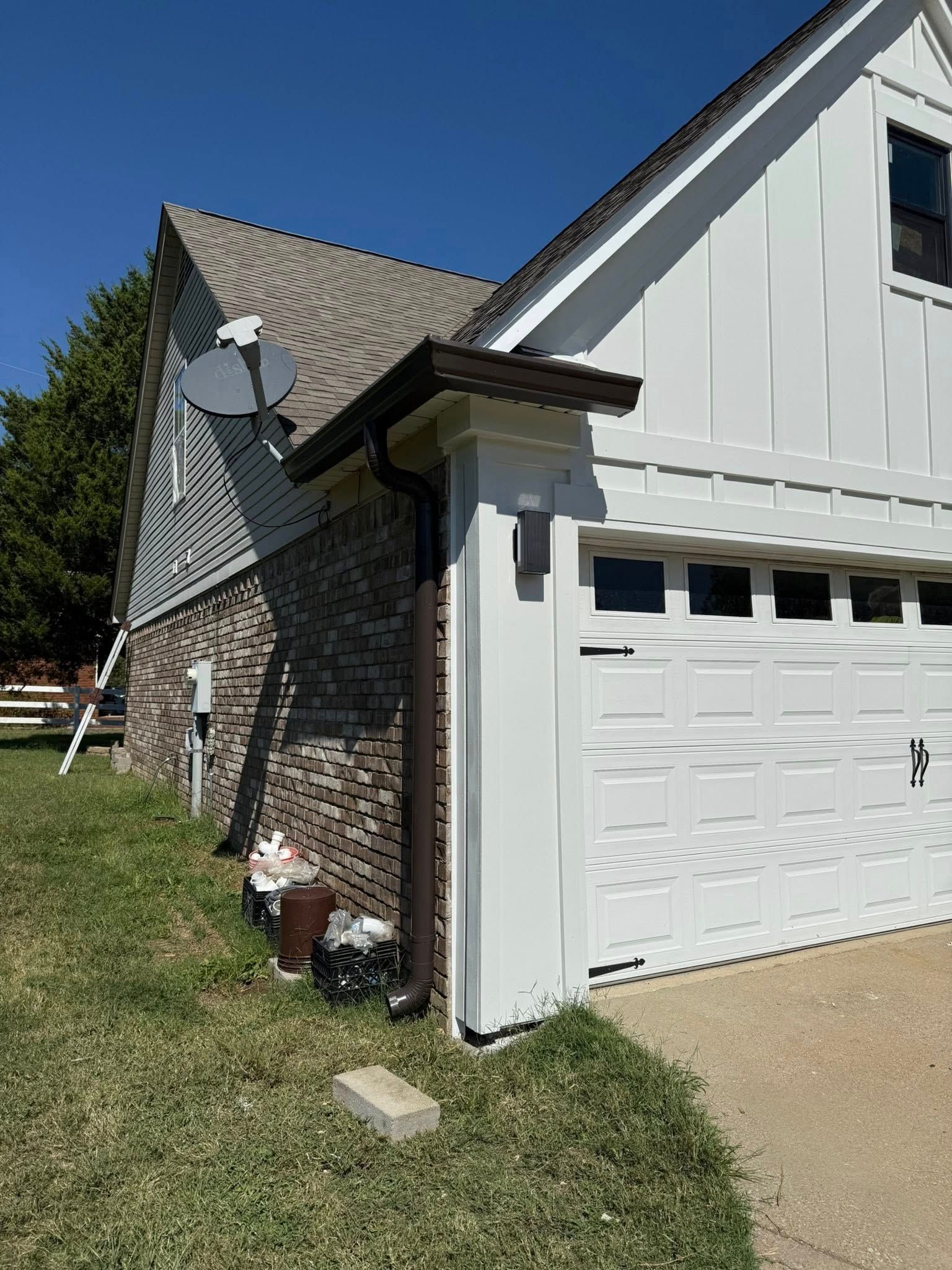 Exterior of a house with brick and white siding, a garage door, satellite dish, and grassy yard