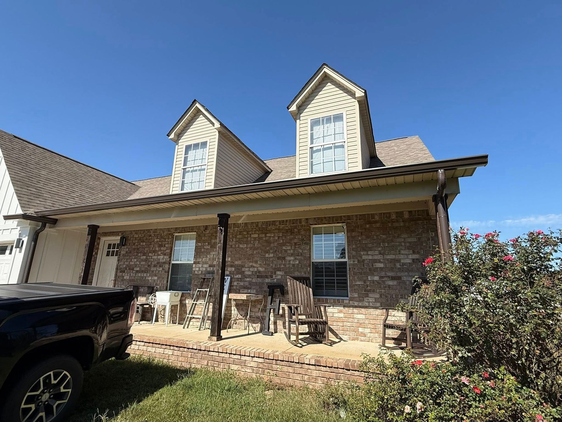 Brick house with a covered porch and two dormer windows under a blue sky