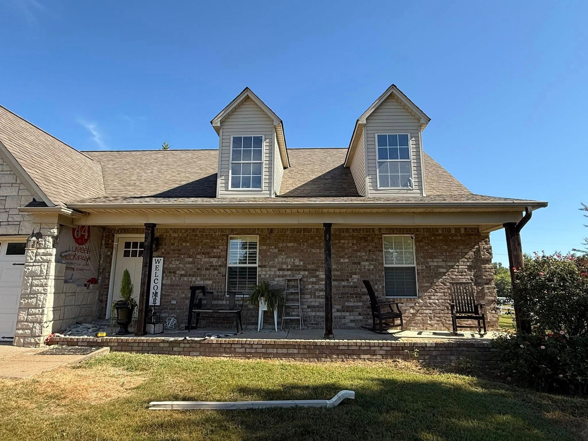 Stone house with a covered front porch, two dormer windows, and a grassy yard under a blue sky