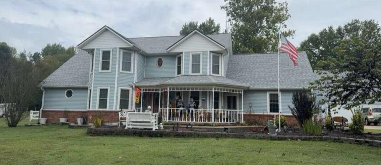 Gray two-story house with a front porch and an American flag on a grassy lot