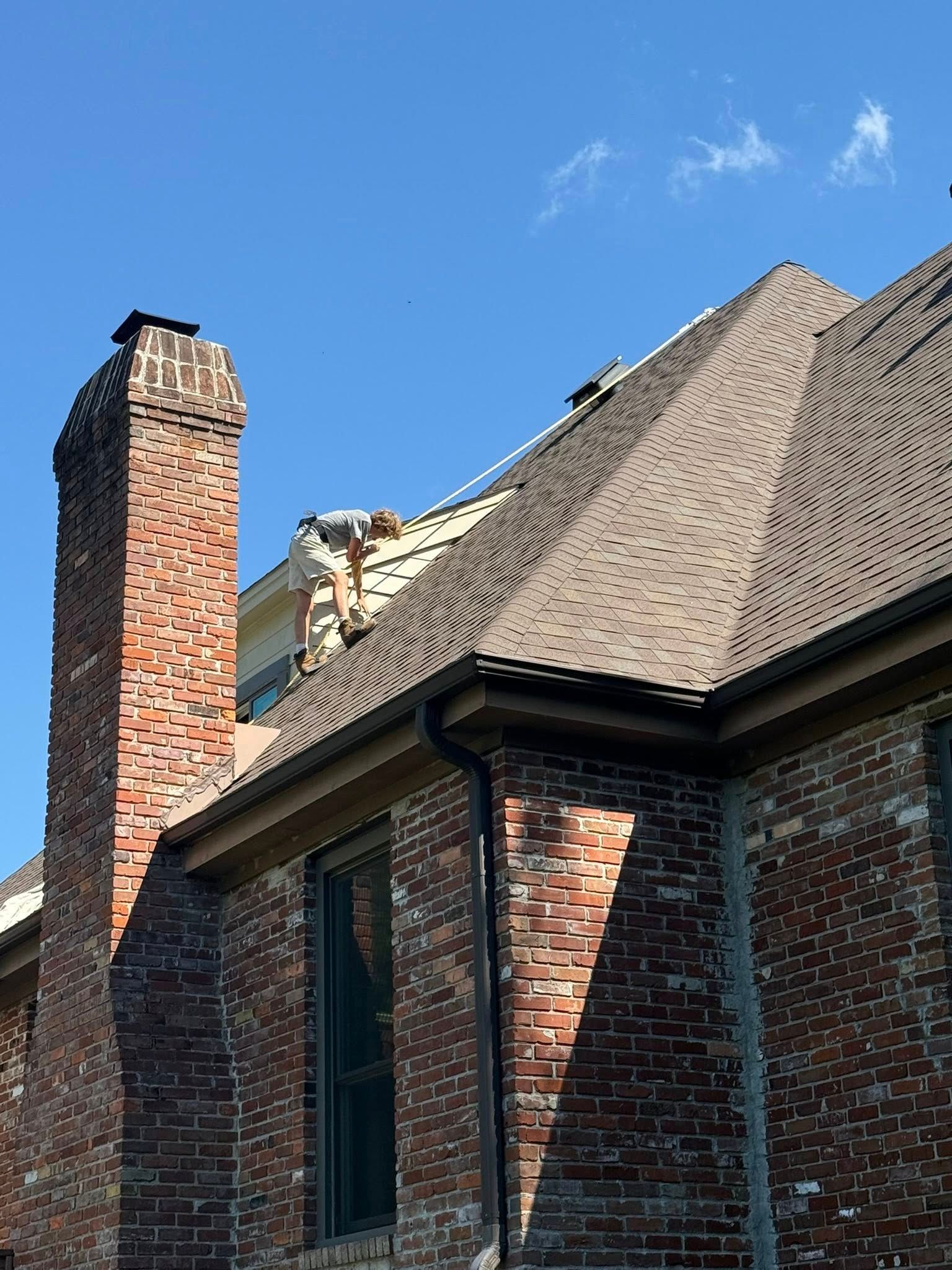 Brick house chimney and shingled roof against a clear blue sky