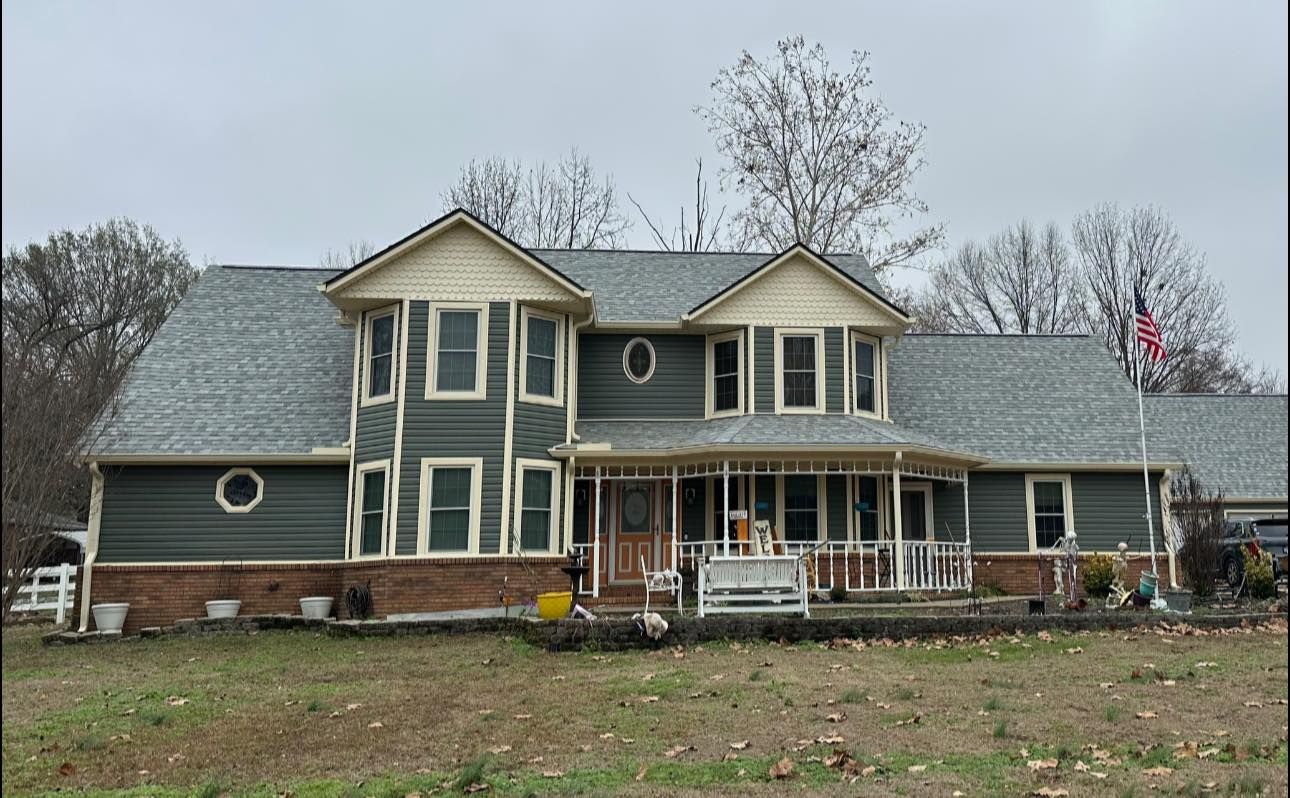 Large two-story gray house with white trim and a covered front porch on an overcast day