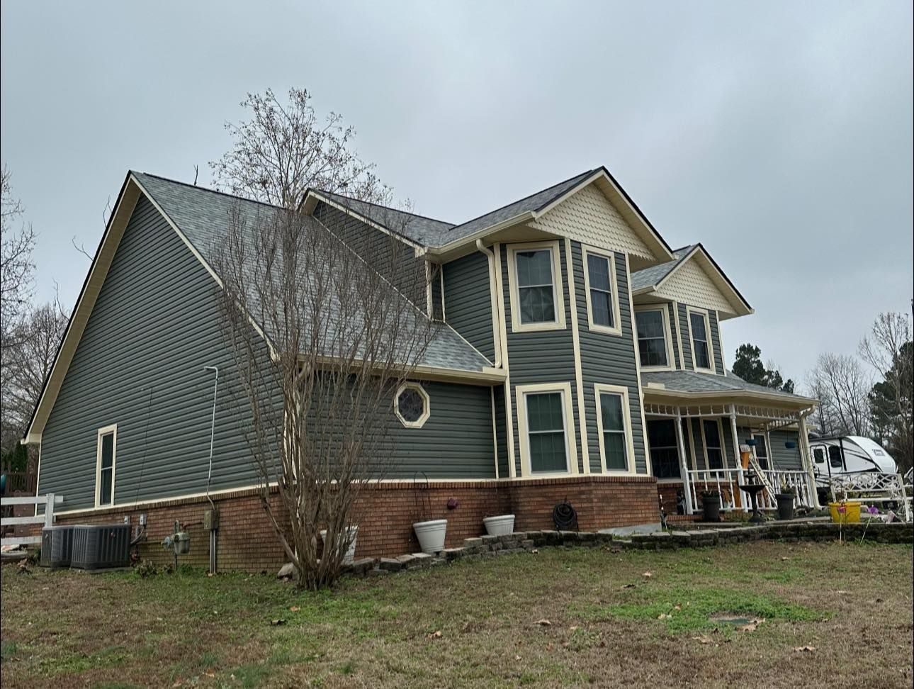 Two-story blue house with brick foundation and screened porch on a cloudy day