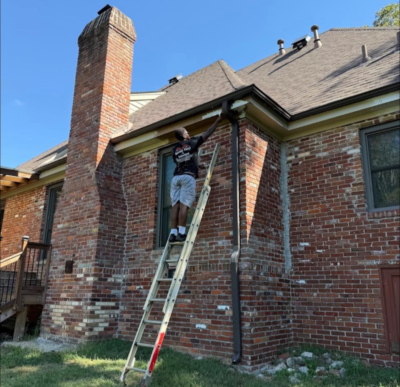 Worker on a ladder repairing the roofline of a brick house on a sunny day