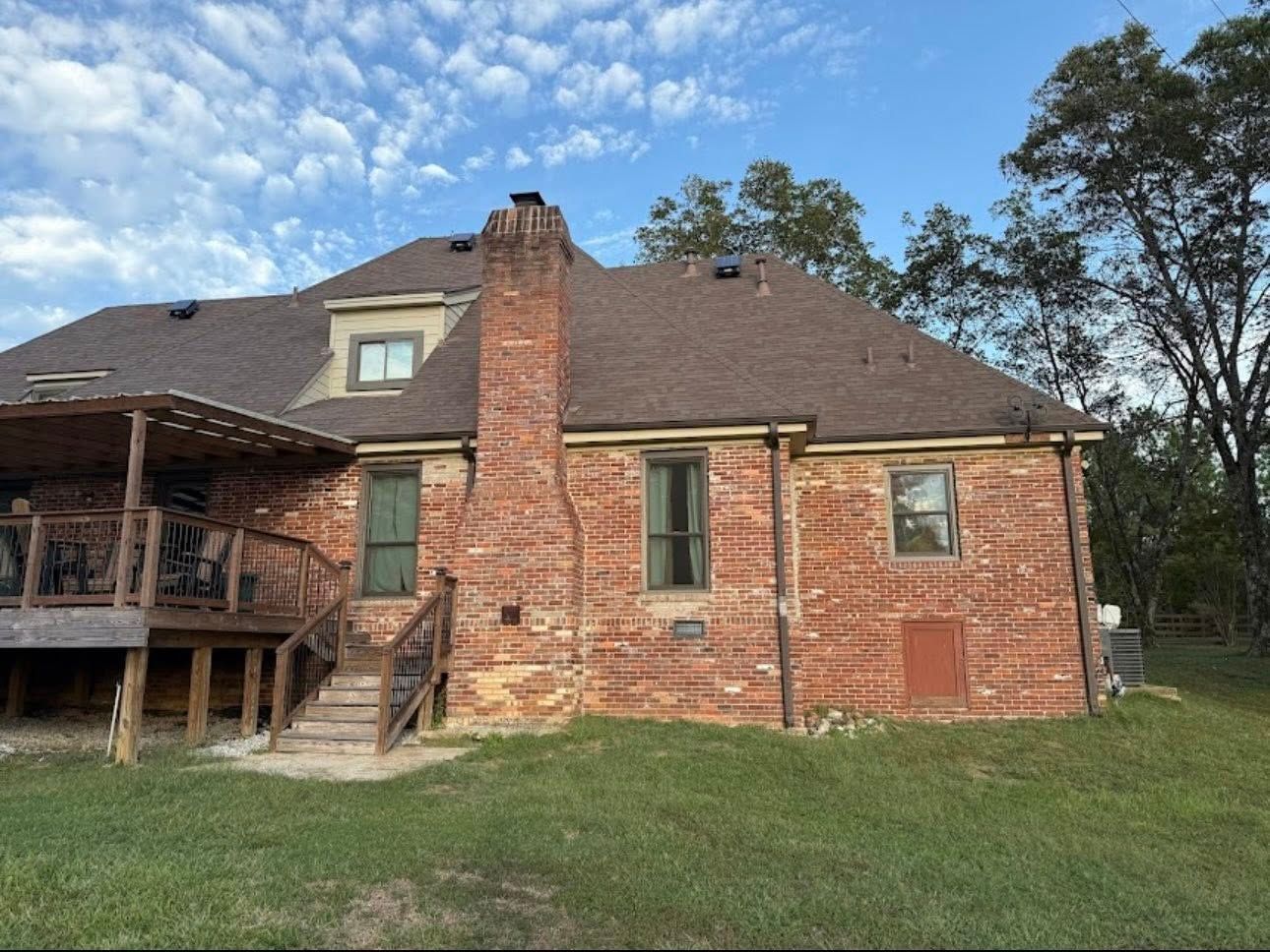 Brick house with a screened porch, dormer window, and brick chimney under a cloudy blue sky.