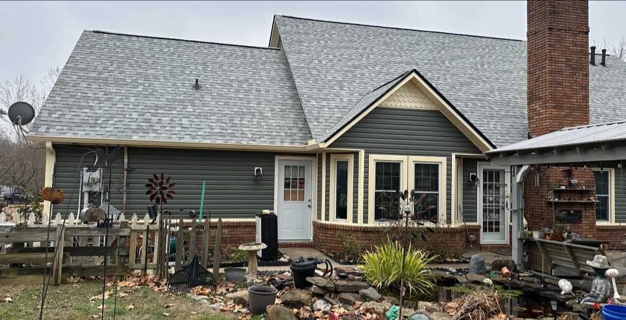 House exterior with gray roof, brick chimney, and landscaped front yard in a rainy setting