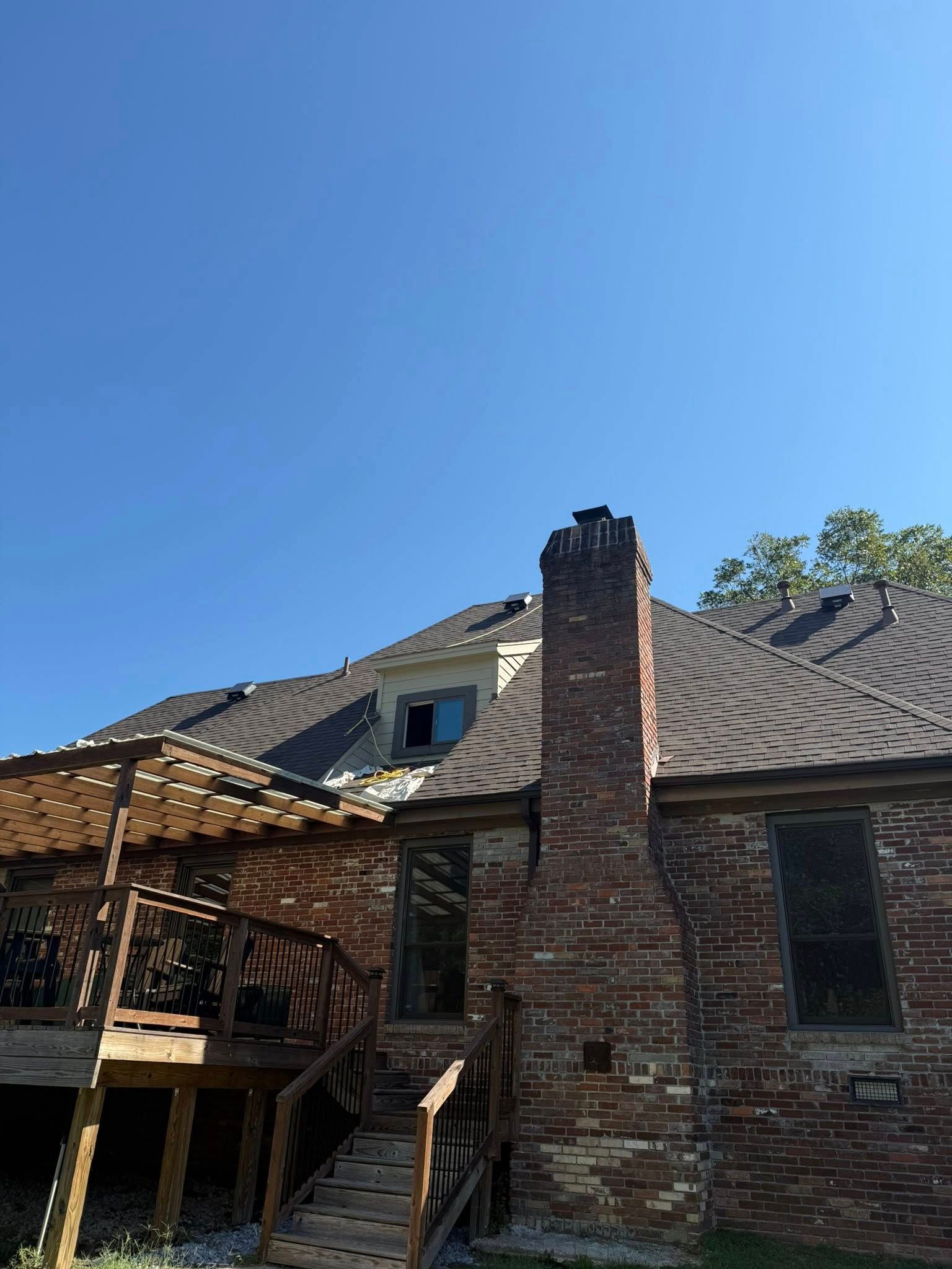 Brick house with damaged roof and chimney beneath a clear blue sky