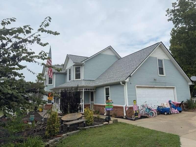 Suburban house with light blue siding, driveway, porch, and toys scattered near the garage